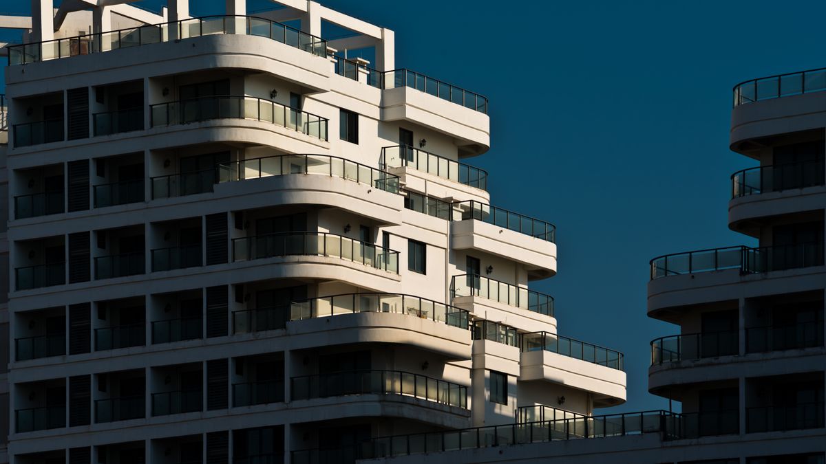 Modern residential apartment building with glass balconies glowing in warm sunset light against an evening sky