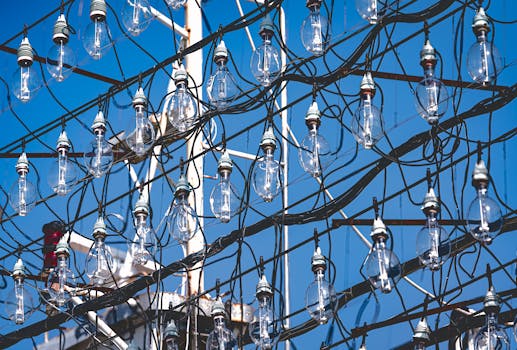 Array of industrial light bulbs hanging against a bright blue sky, showcasing wires and metal structure.