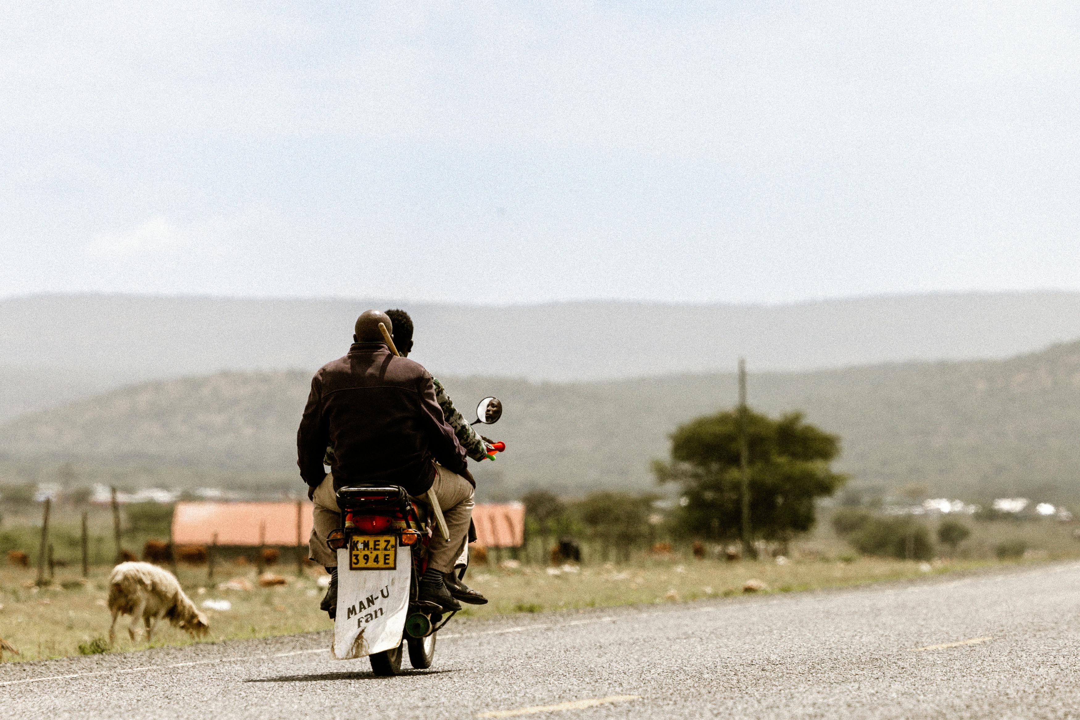 Gratis To personer kører på motorcykel på en landevej, med et smukt landskab i baggrunden. Lagerfoto