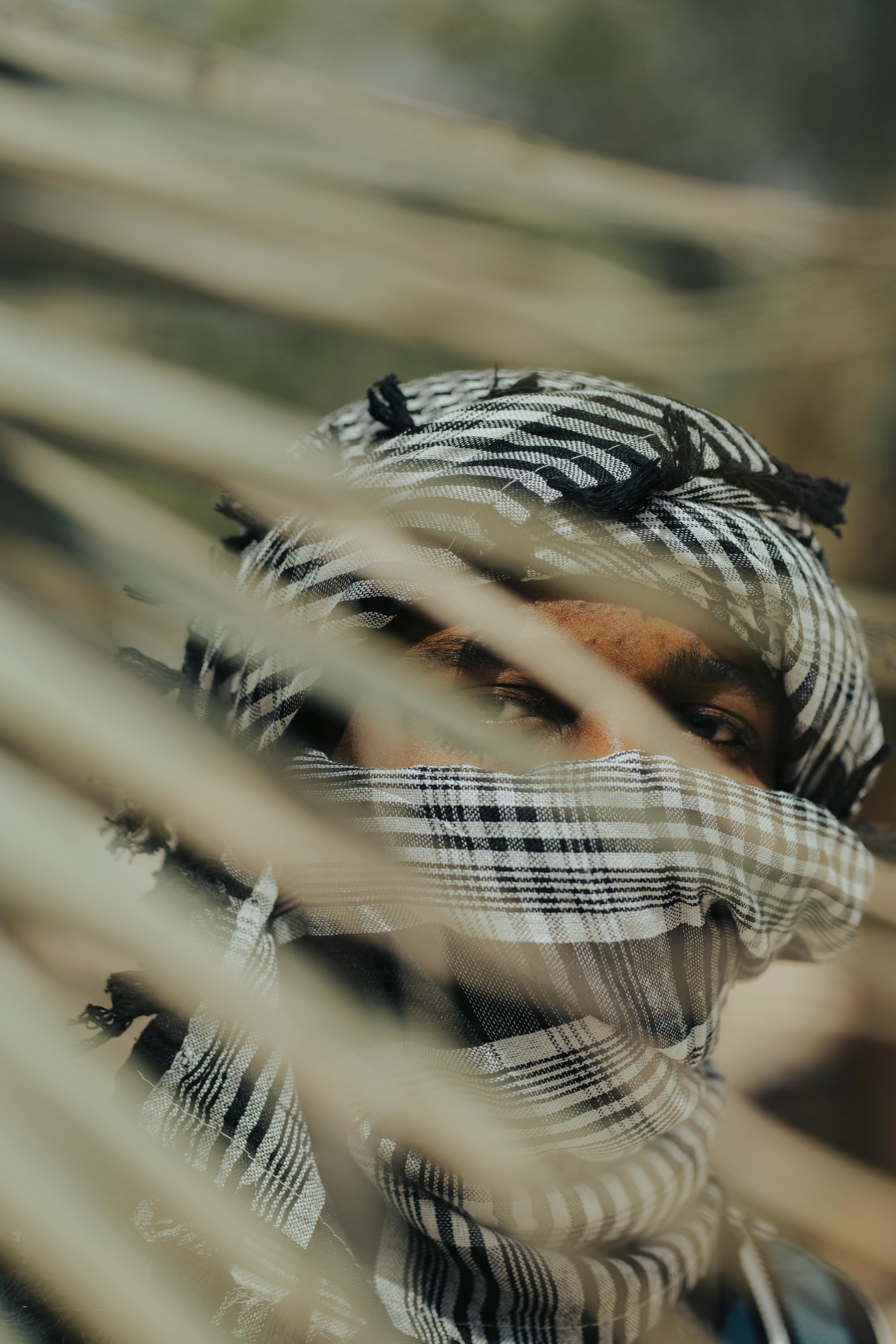 Gratis En person delvis skjult bak palmeblader, iført et mønstret hodeskjerf i Kano, Nigeria. Arkivbilde