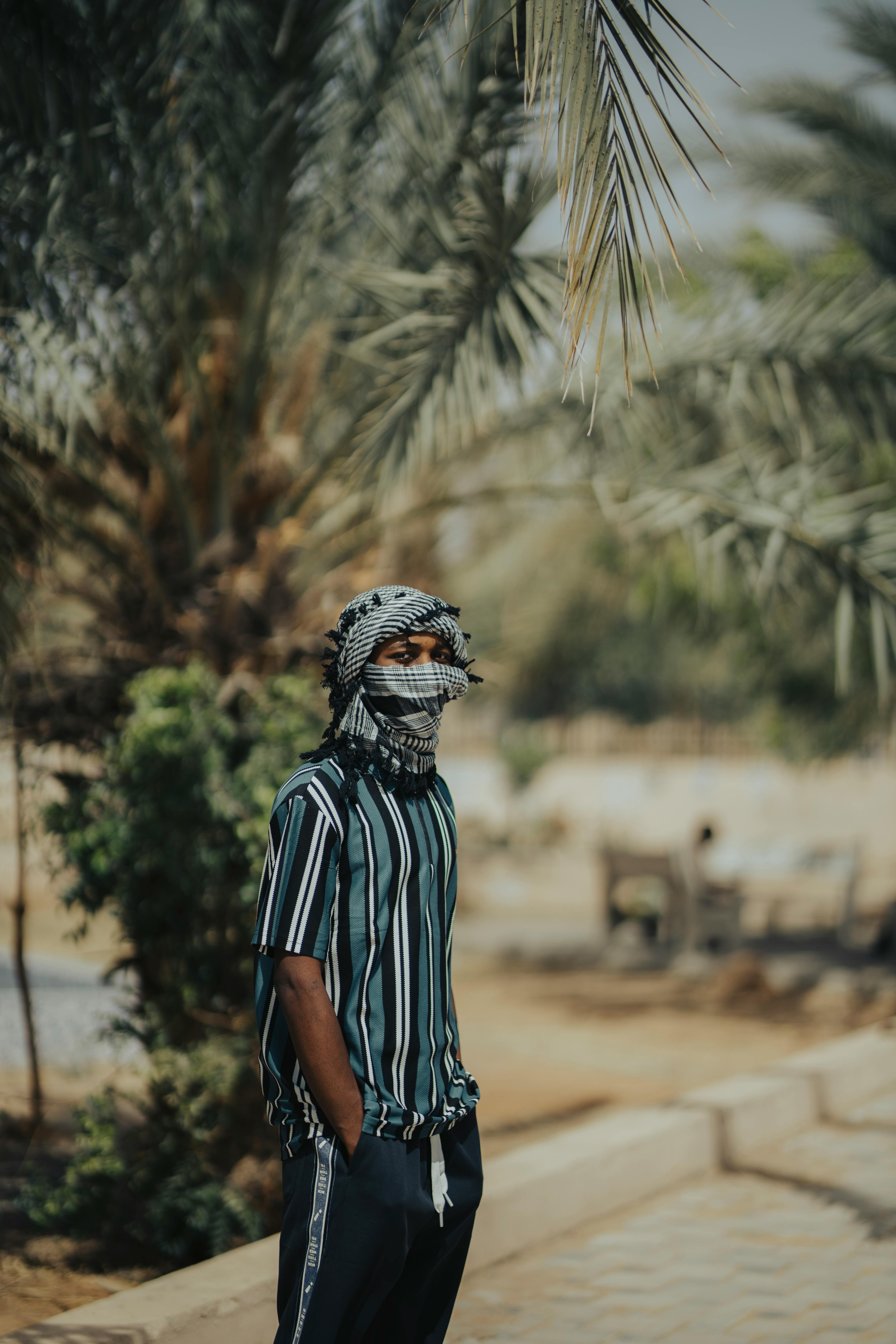 Gratis Ung mann i tradisjonell drakt står under palmer i Kano, Nigeria, og foreviger et fredfylt øyeblikk. Arkivbilde