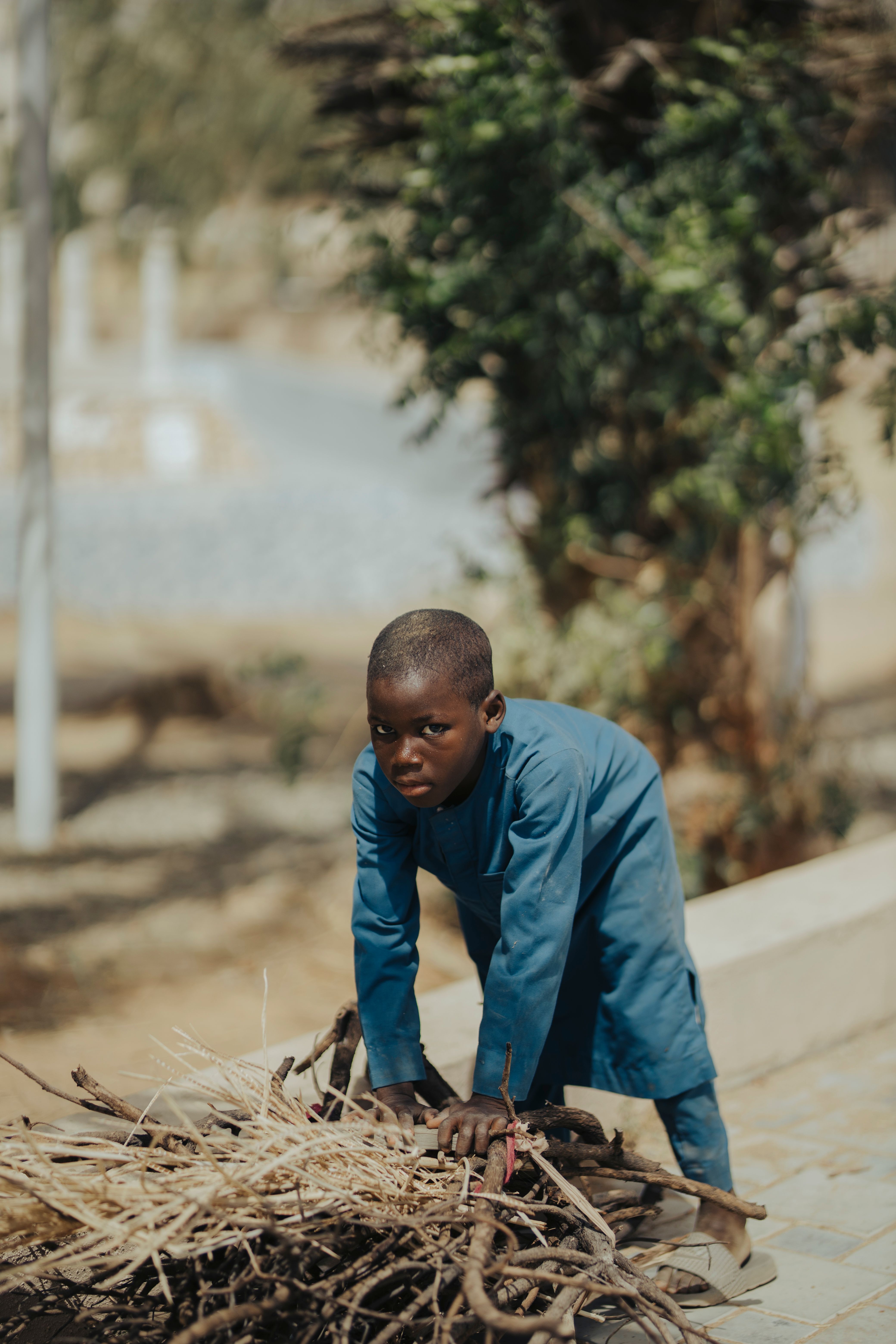 A young boy in traditional attire gathers firewood outdoors in Kano, Nigeria.