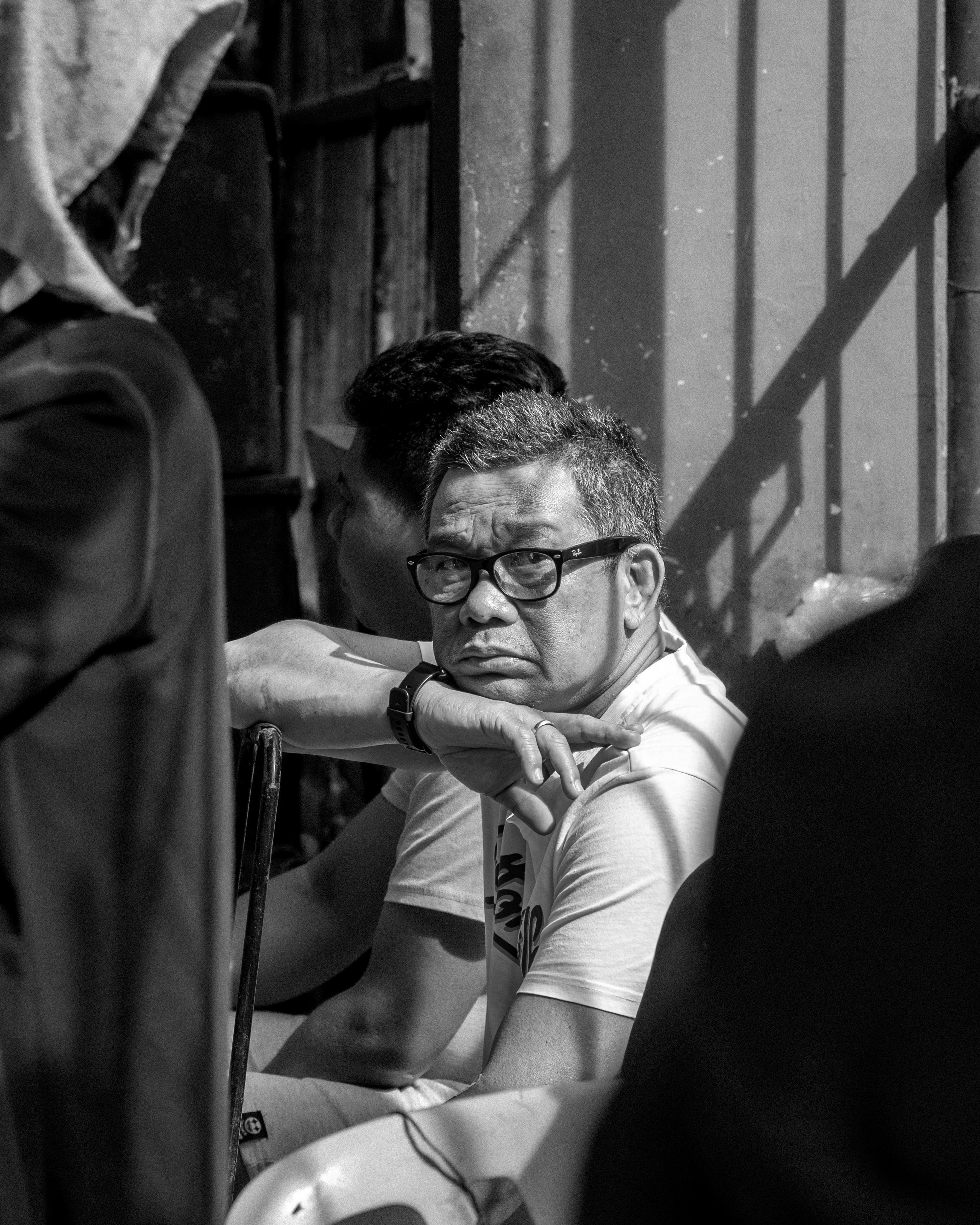 бесплатная На черно-белой фотографии задумчивый мужчина сидит на открытом воздухе. Стоковое фото