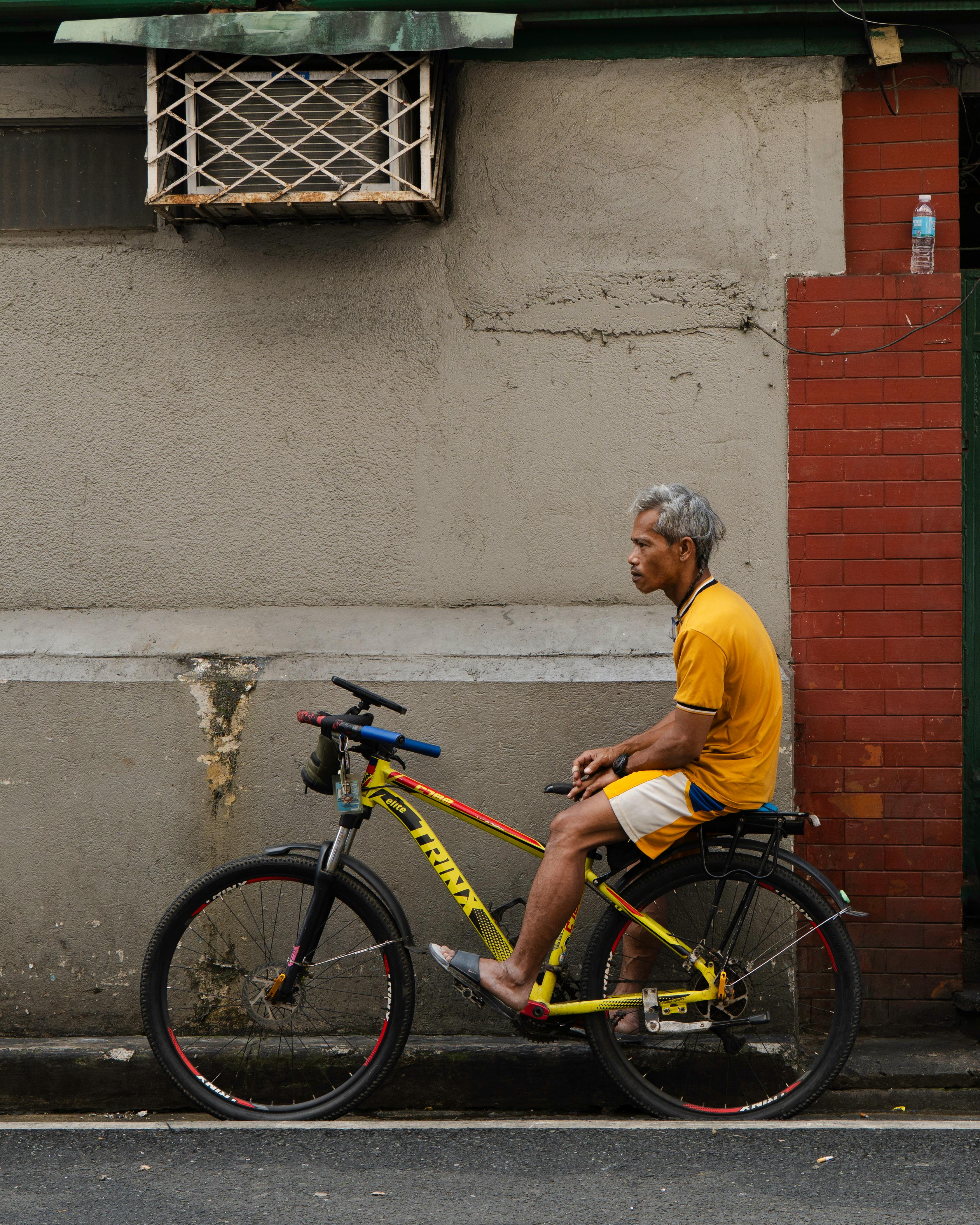 無料 カジュアルな服装の男性が、質感のある城壁を背景に自転車に座り、都会のライフスタイルを披露しています。 写真素材