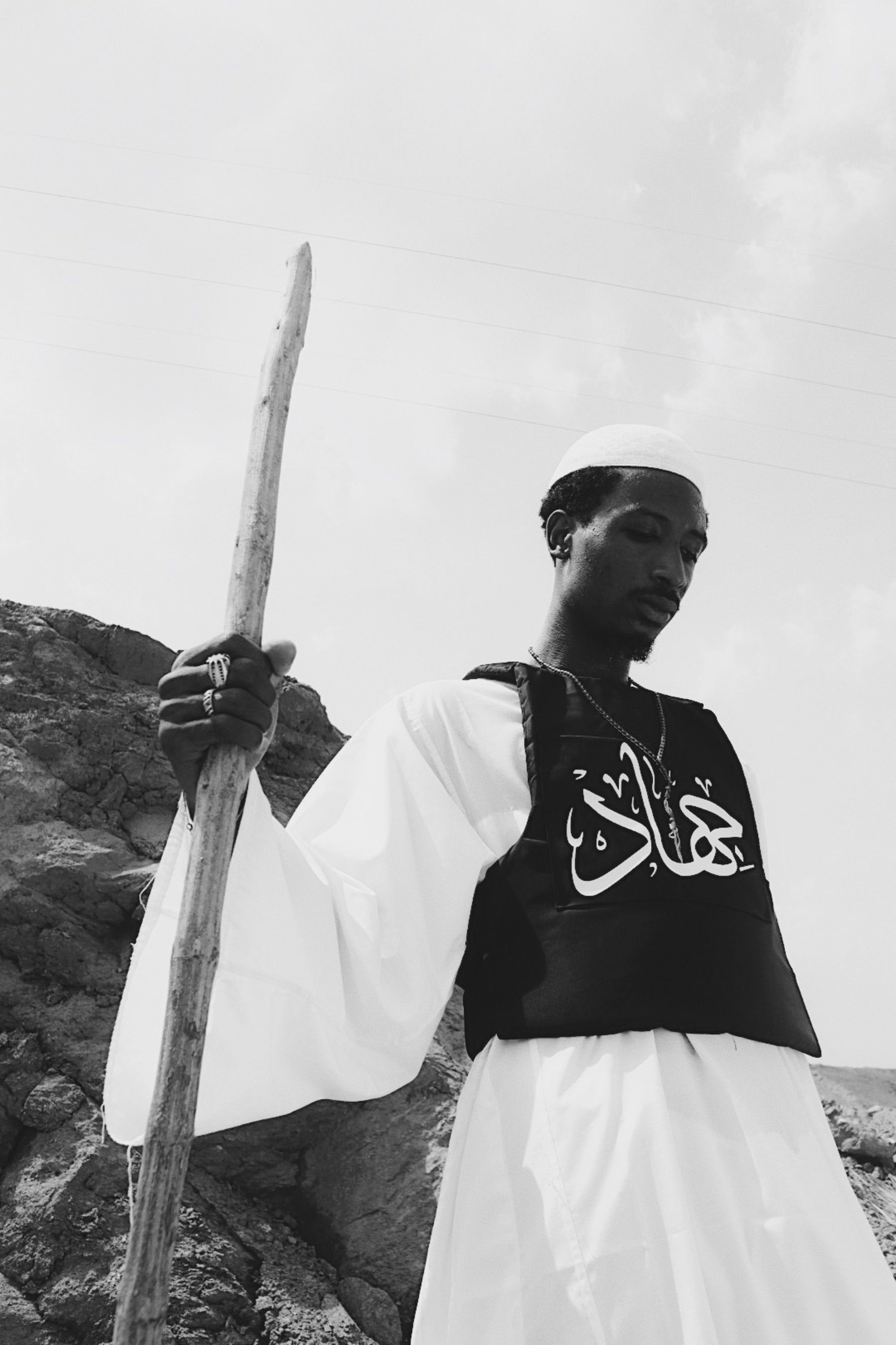 Black and white portrait of a man in traditional attire with a staff.