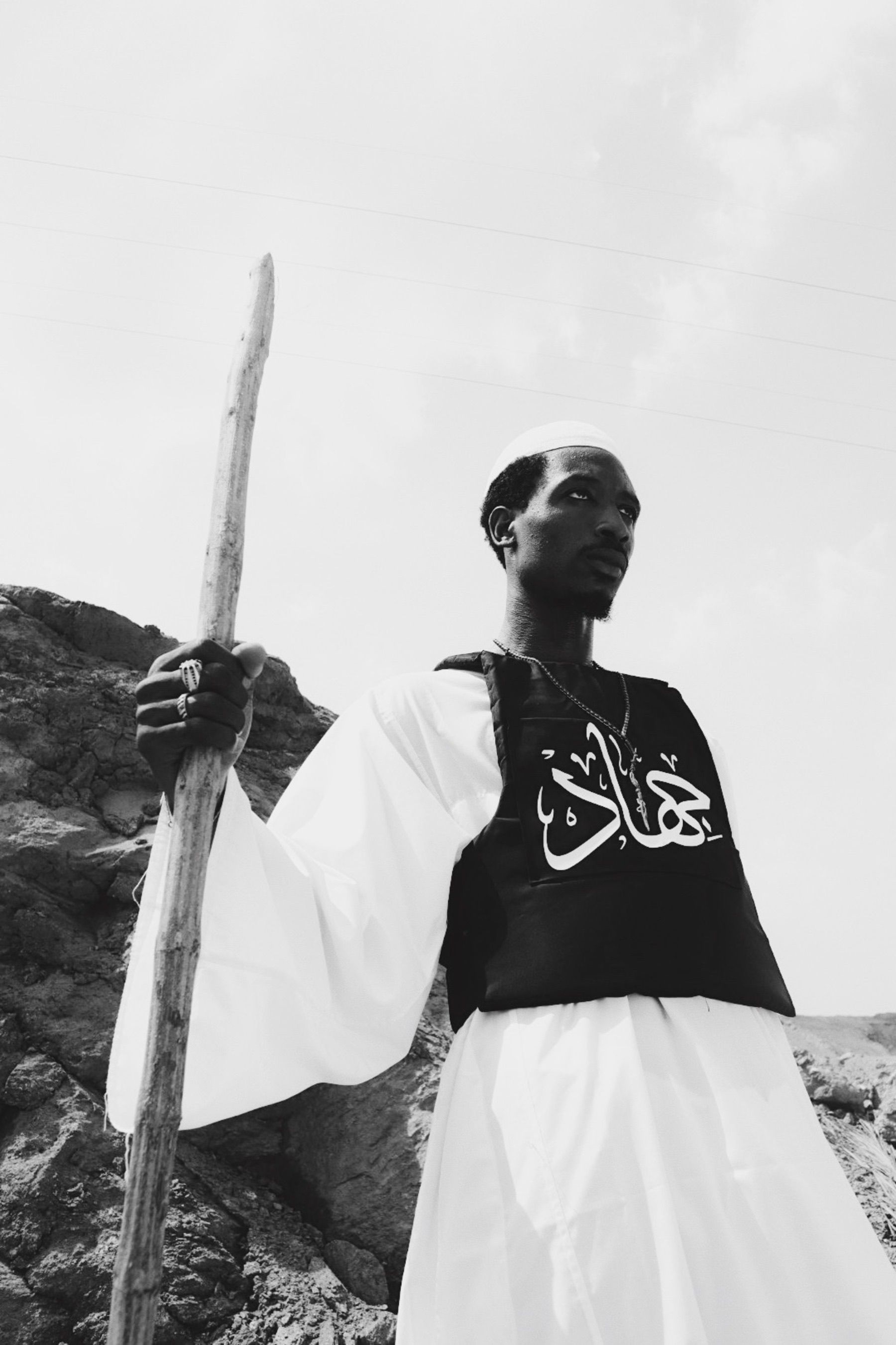 Black and white photo of a man with staff in a desert setting.