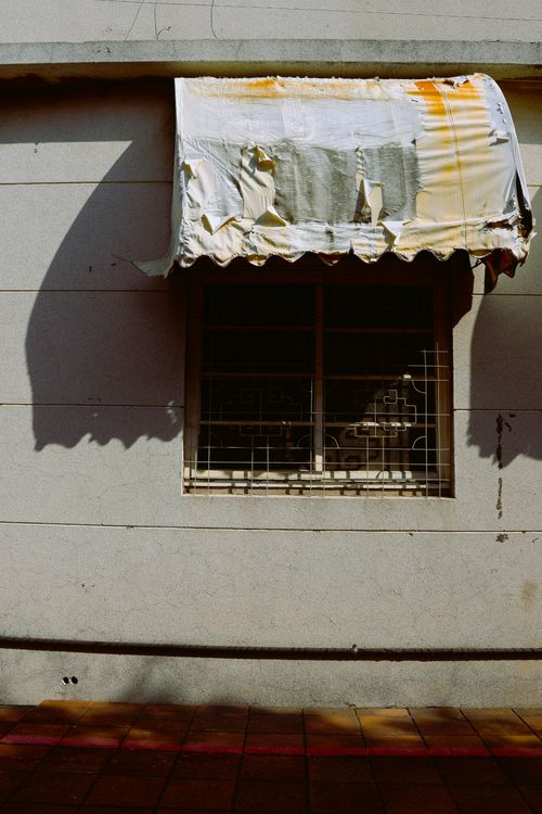 Free An old window with a weathered awning casting shadows on a sunny day. Stock Photo
