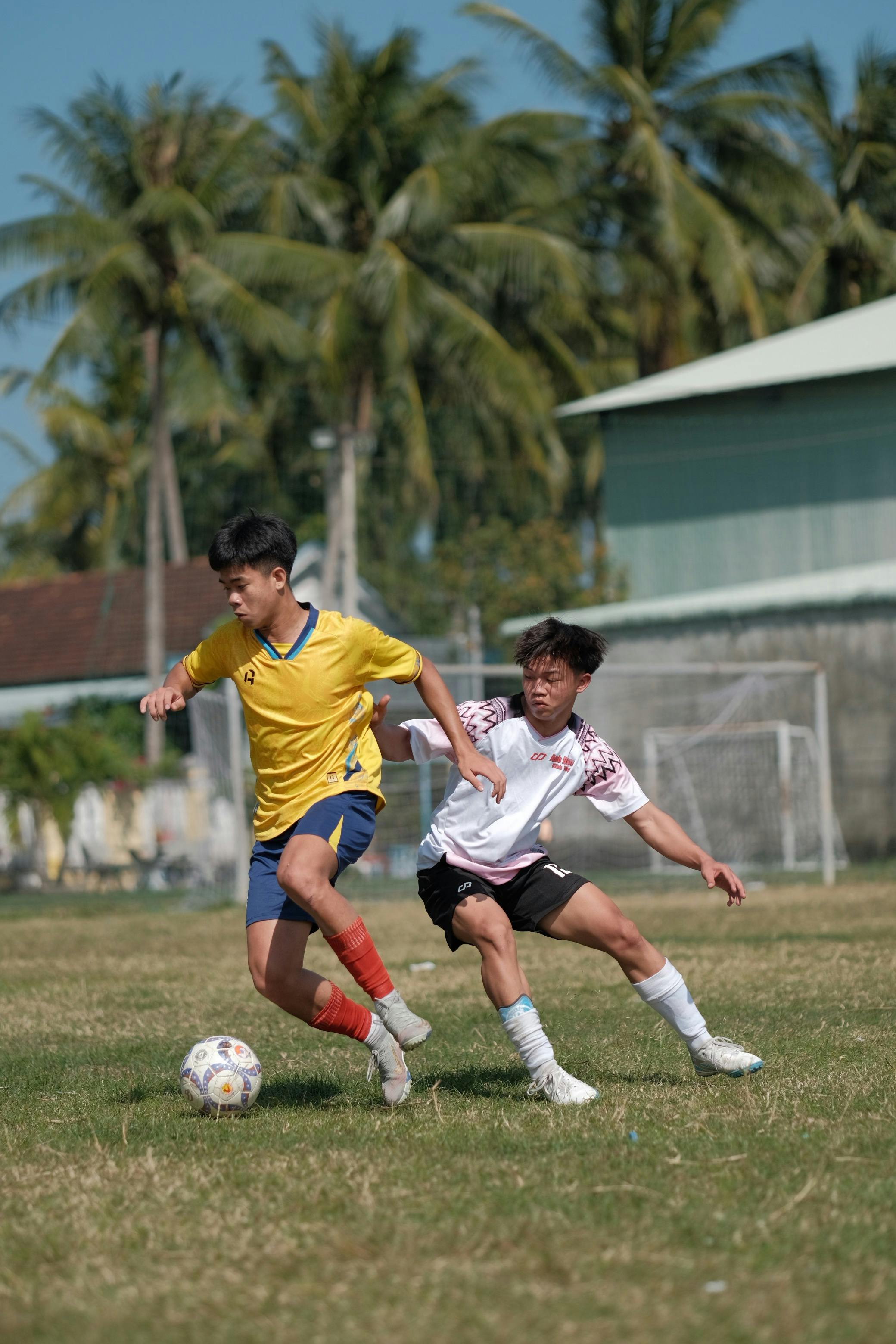 Gratis To tenåringer spiller fotball energisk på en gressbane under palmer. Arkivbilde