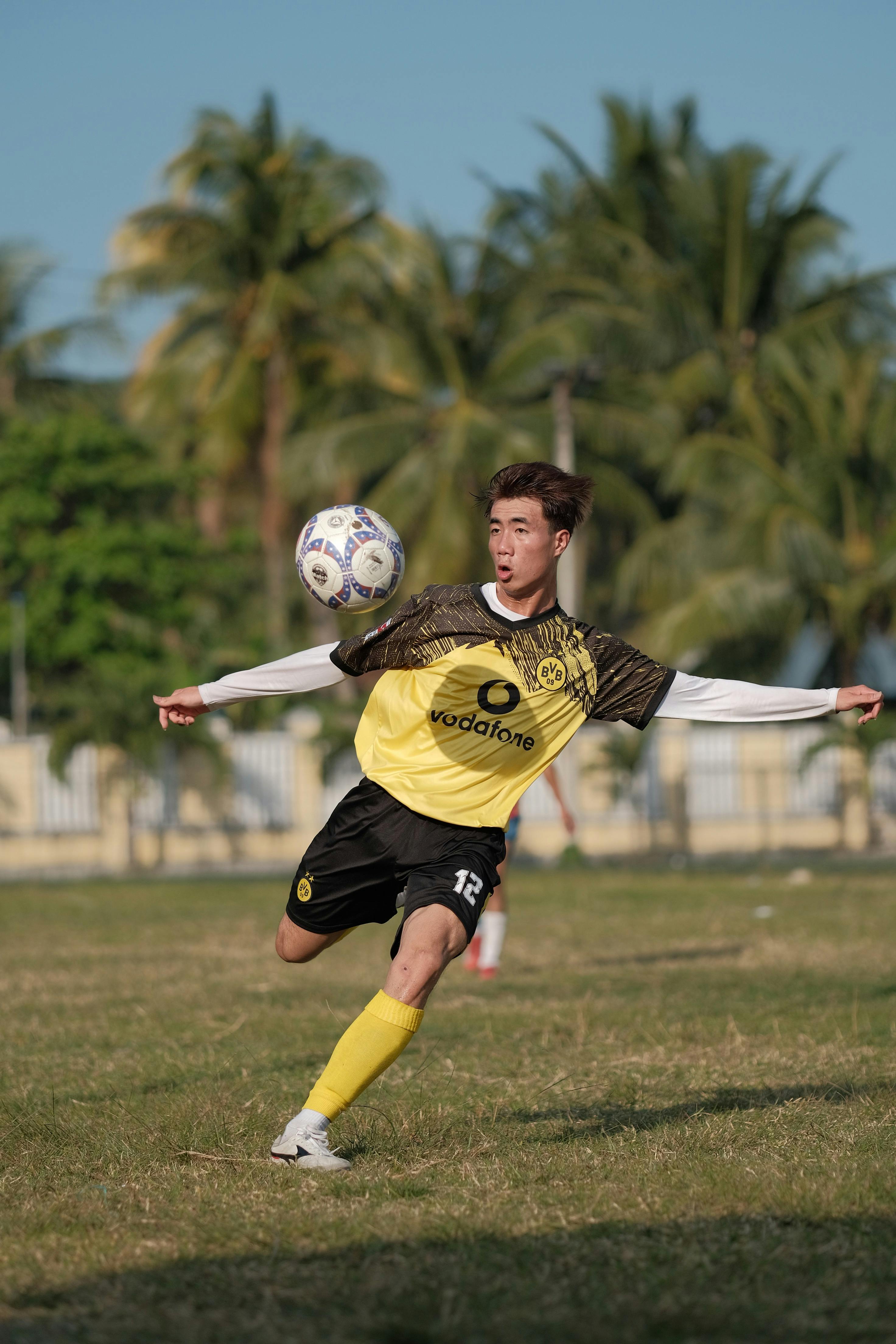 Gratis Actionbillede af en fodboldspiller, der sparker bolden på en solskinsdag udendørs. Lagerfoto