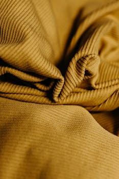 A detailed close-up of textured yellow fabric with soft folds and highlights.