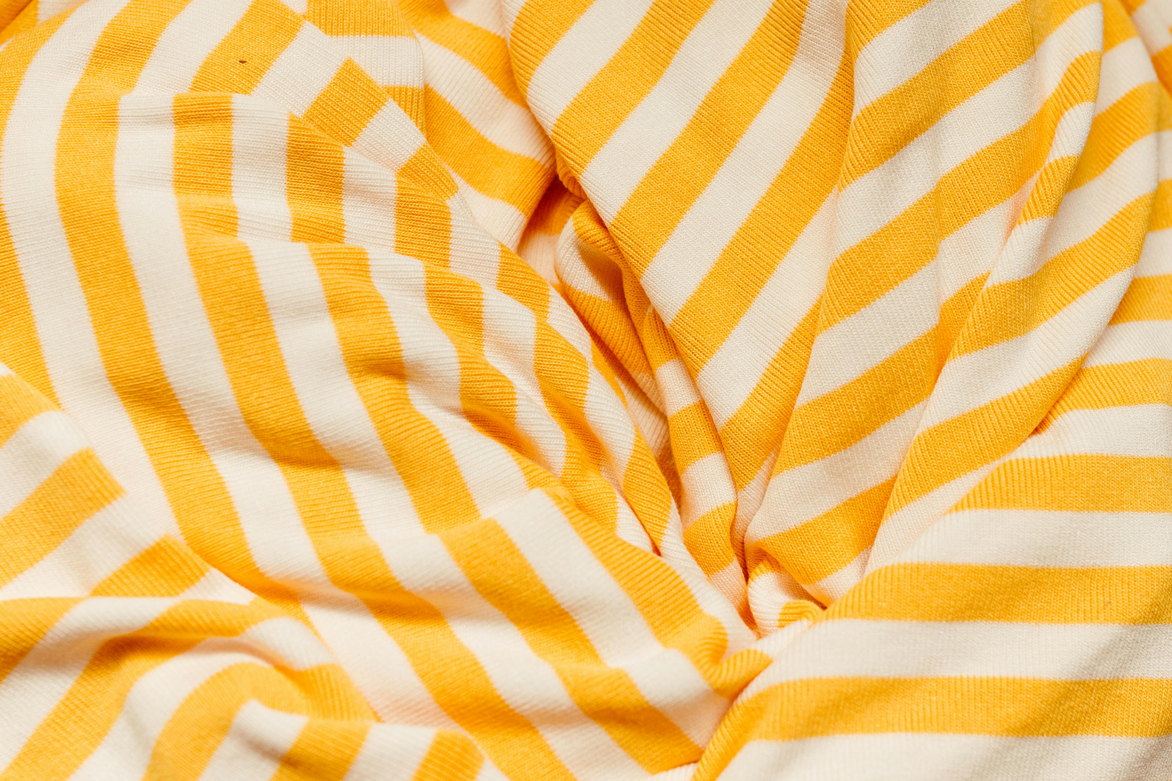 бесплатная Детальный снимок фактурной ткани в желтую и белую полоску, демонстрирующий ее яркий узор. Стоковое фото