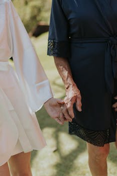Two women wearing robes holding hands outdoors, symbolizing connection and support under sunlight.