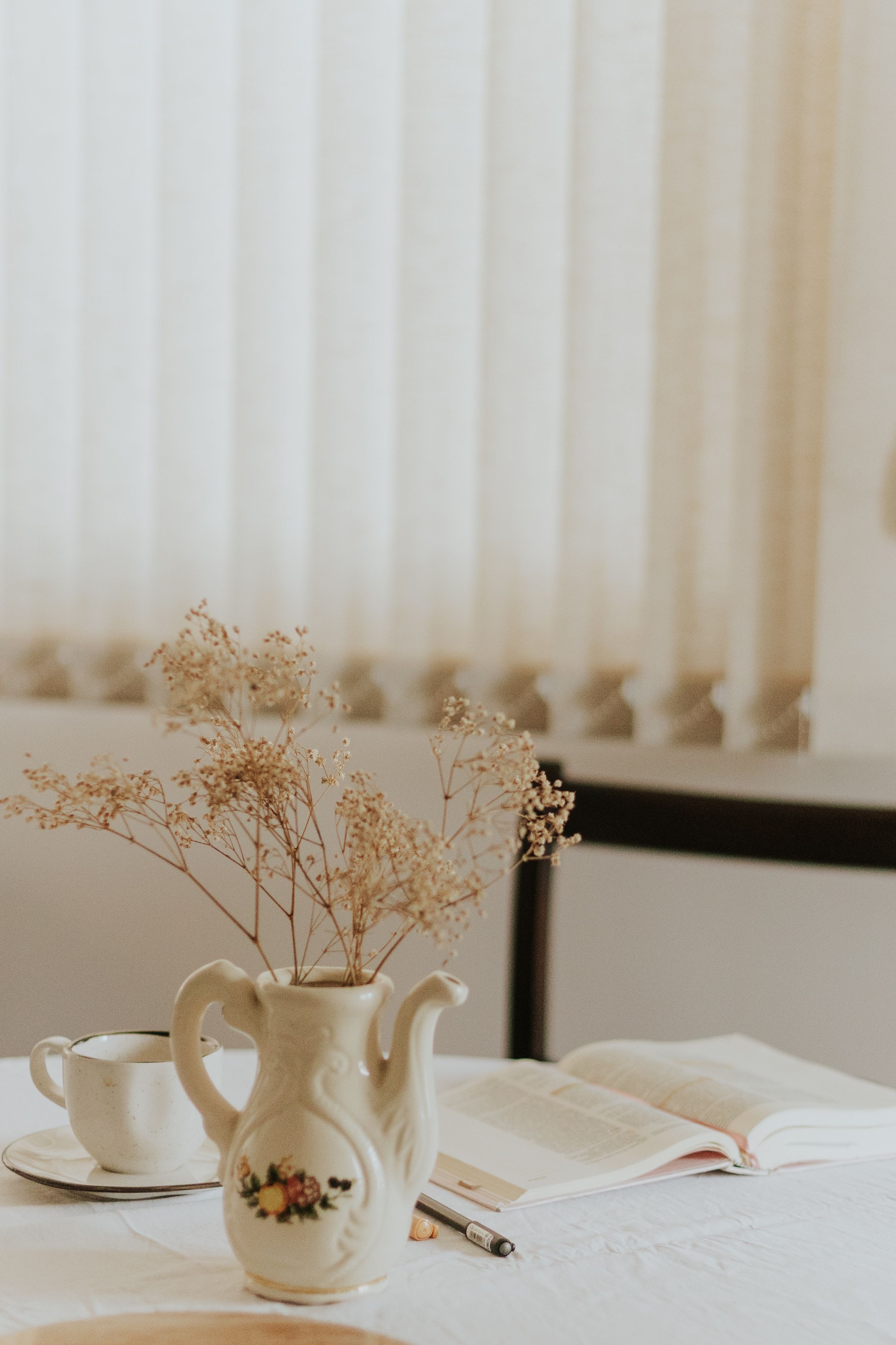 Cena minimalista em ambiente interno com vaso de flores e livro aberto, criando uma atmosfera aconchegante.