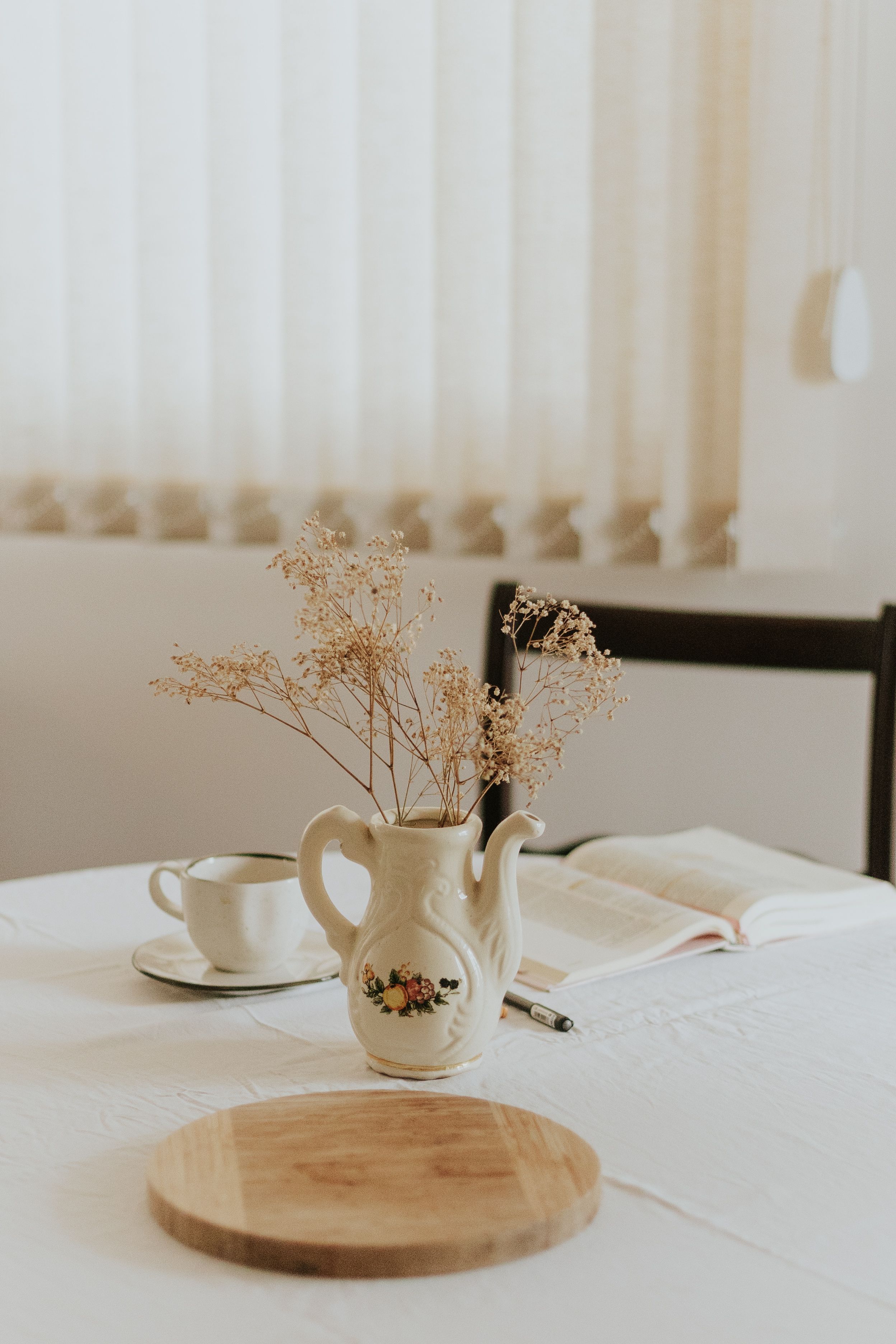 Mesa de jantar minimalista e aconchegante com vaso de cerâmica e flores secas, iluminação natural quente.