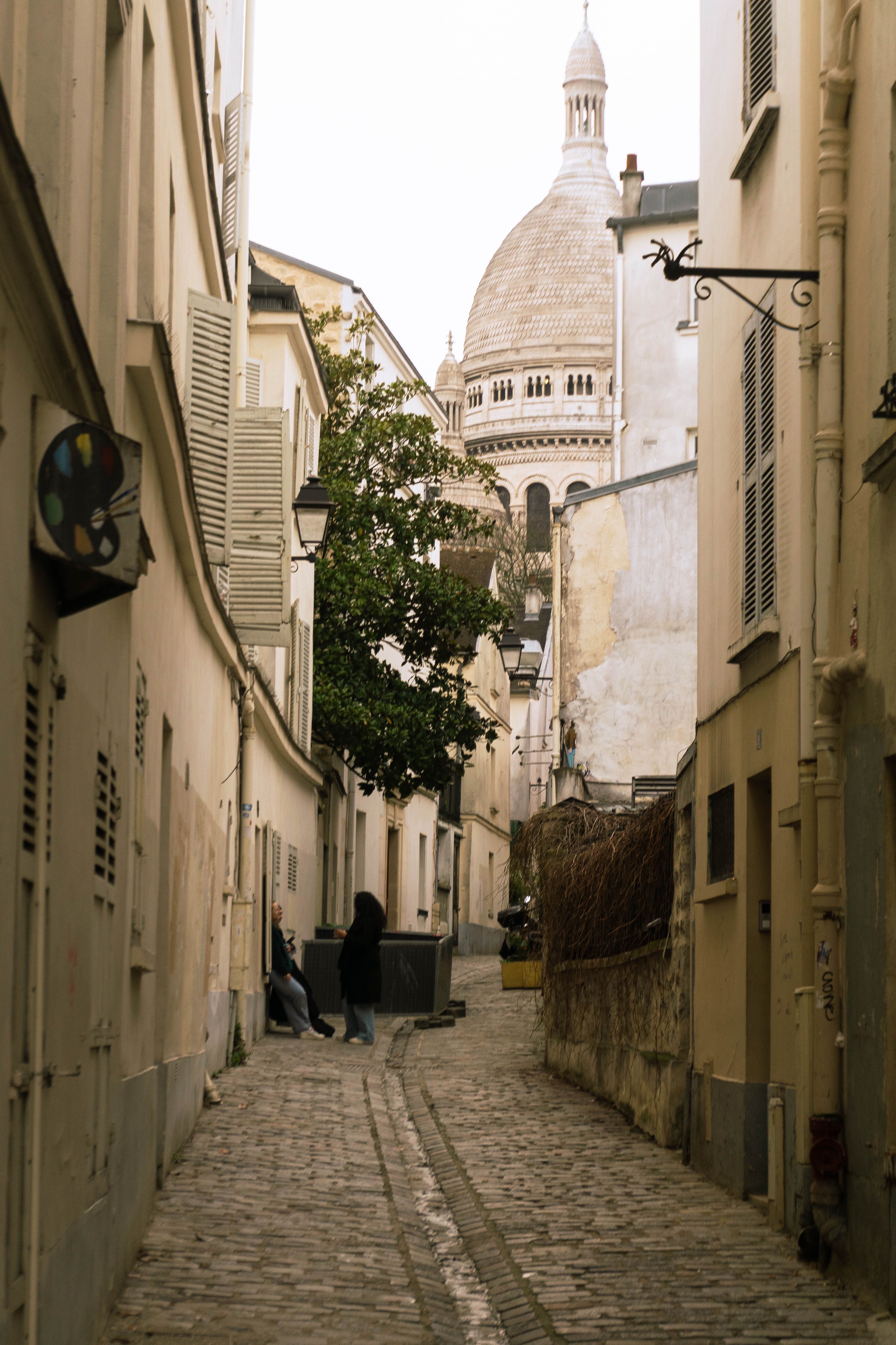 A narrow cobbled lane between shuttered houses, with a white domed basilica at its end