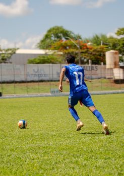 Male soccer player in blue 17 jersey dribbles on sunny green field during daytime match.