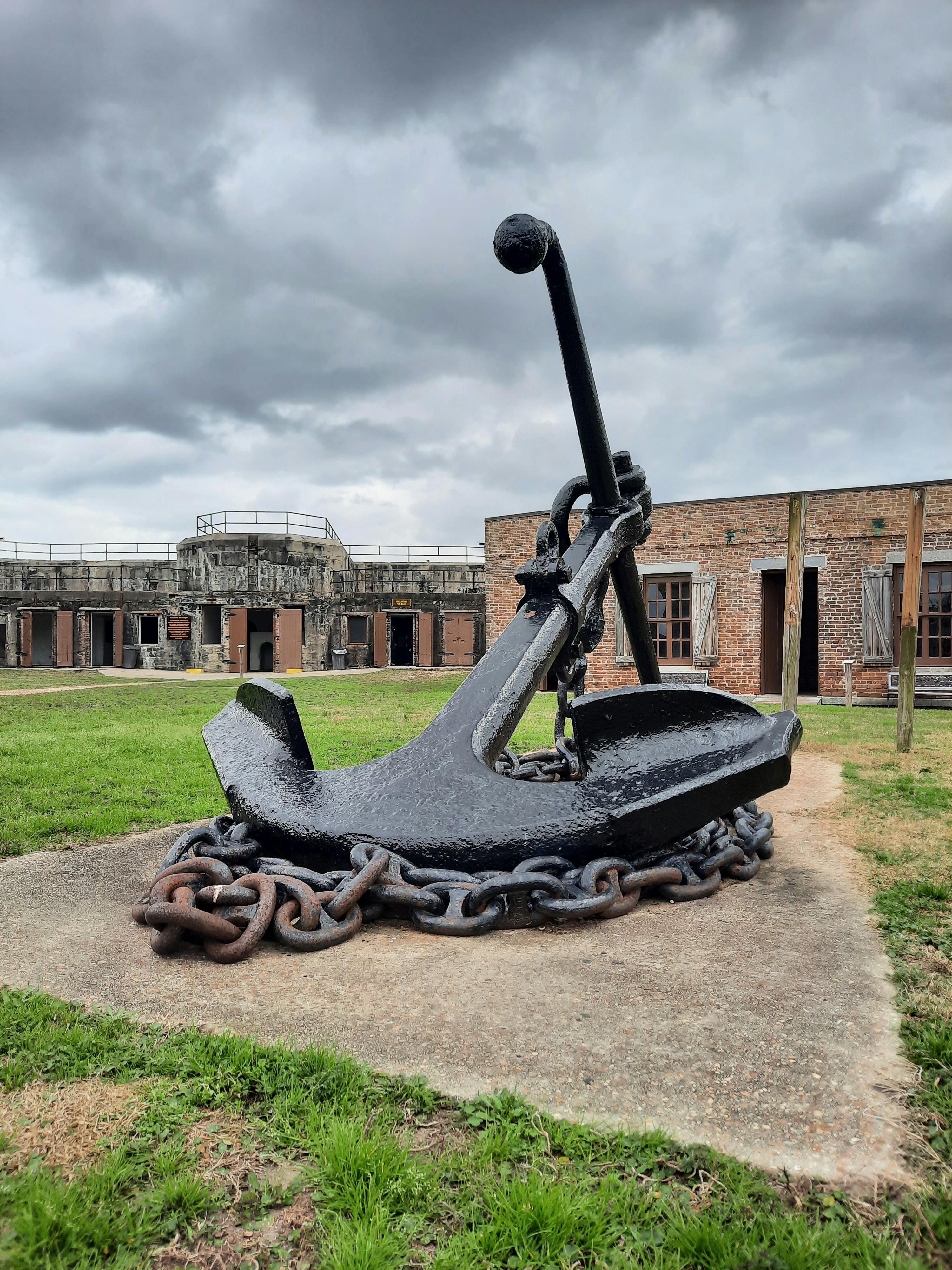 Gratis Jangkar bersejarah berukuran besar dipajang di benteng tua di bawah langit berawan. Foto Stok