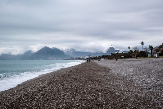 Serene coastal landscape featuring a rocky beach with distant mountains under a cloudy sky.
