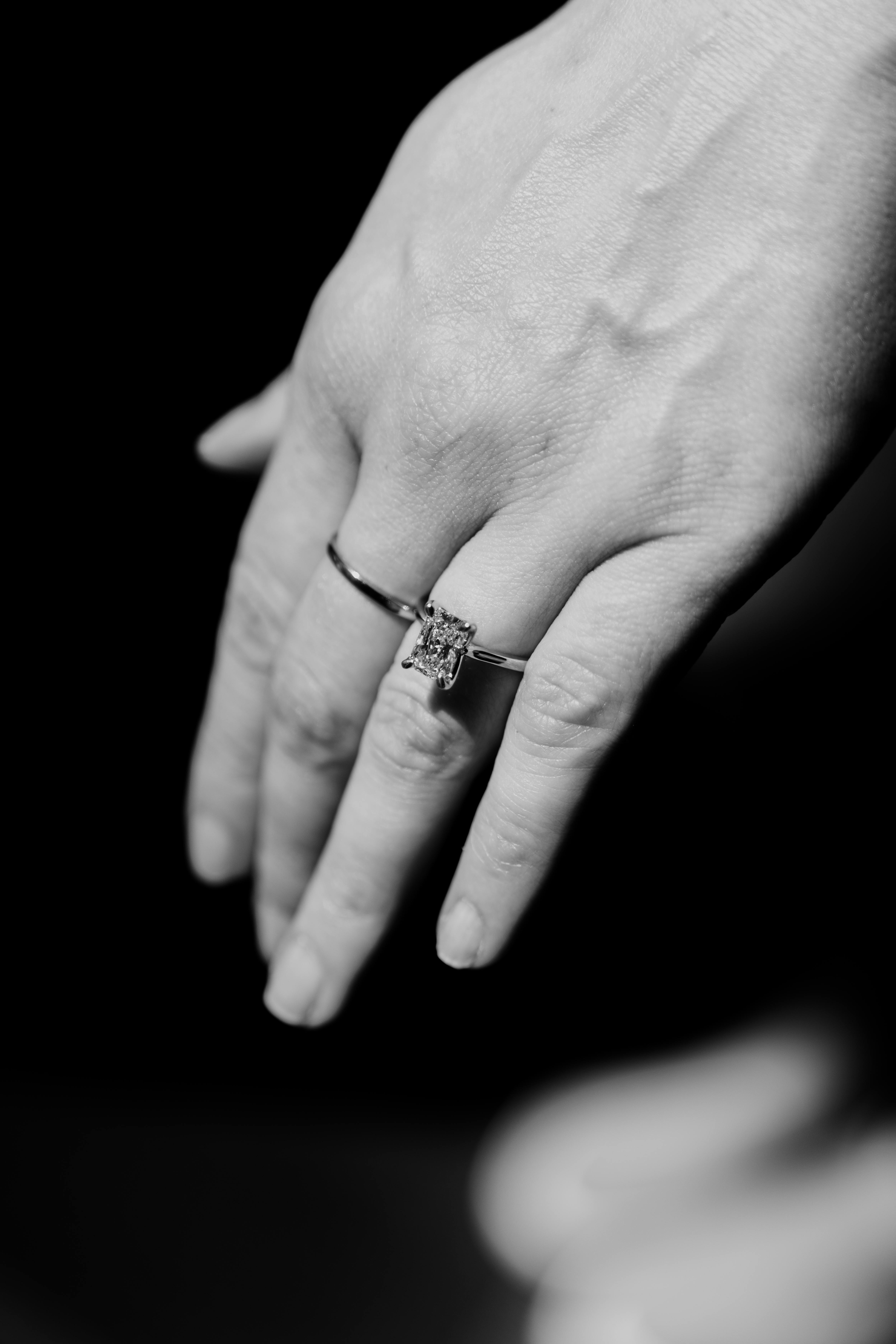 Free Black and white close-up of a hand wearing a diamond engagement ring, conveying elegance and sophistication. Stock Photo