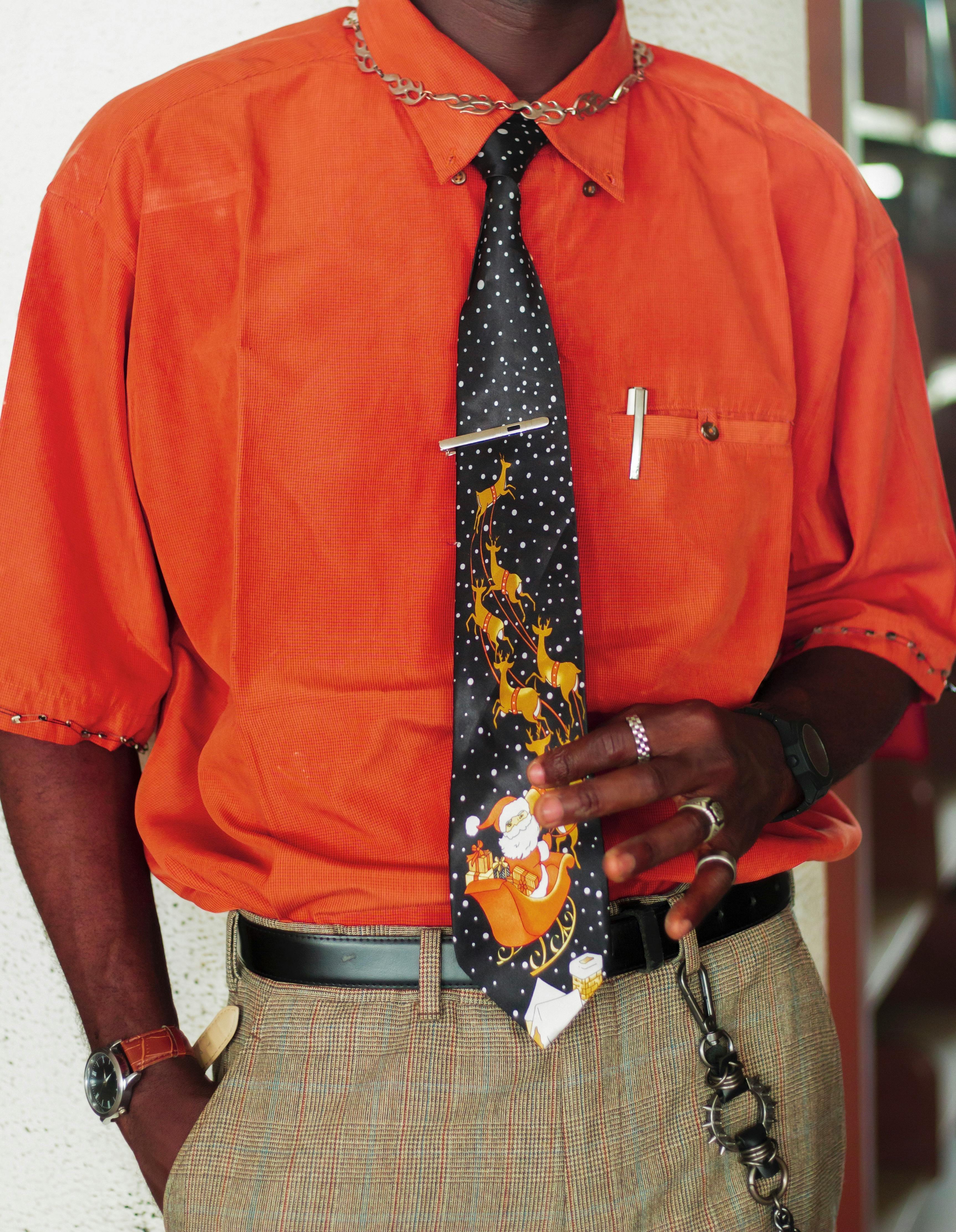 бесплатная Мужчина в ярко-оранжевой рубашке и рождественском галстуке с изображением Санты, стильный образ. Стоковое фото