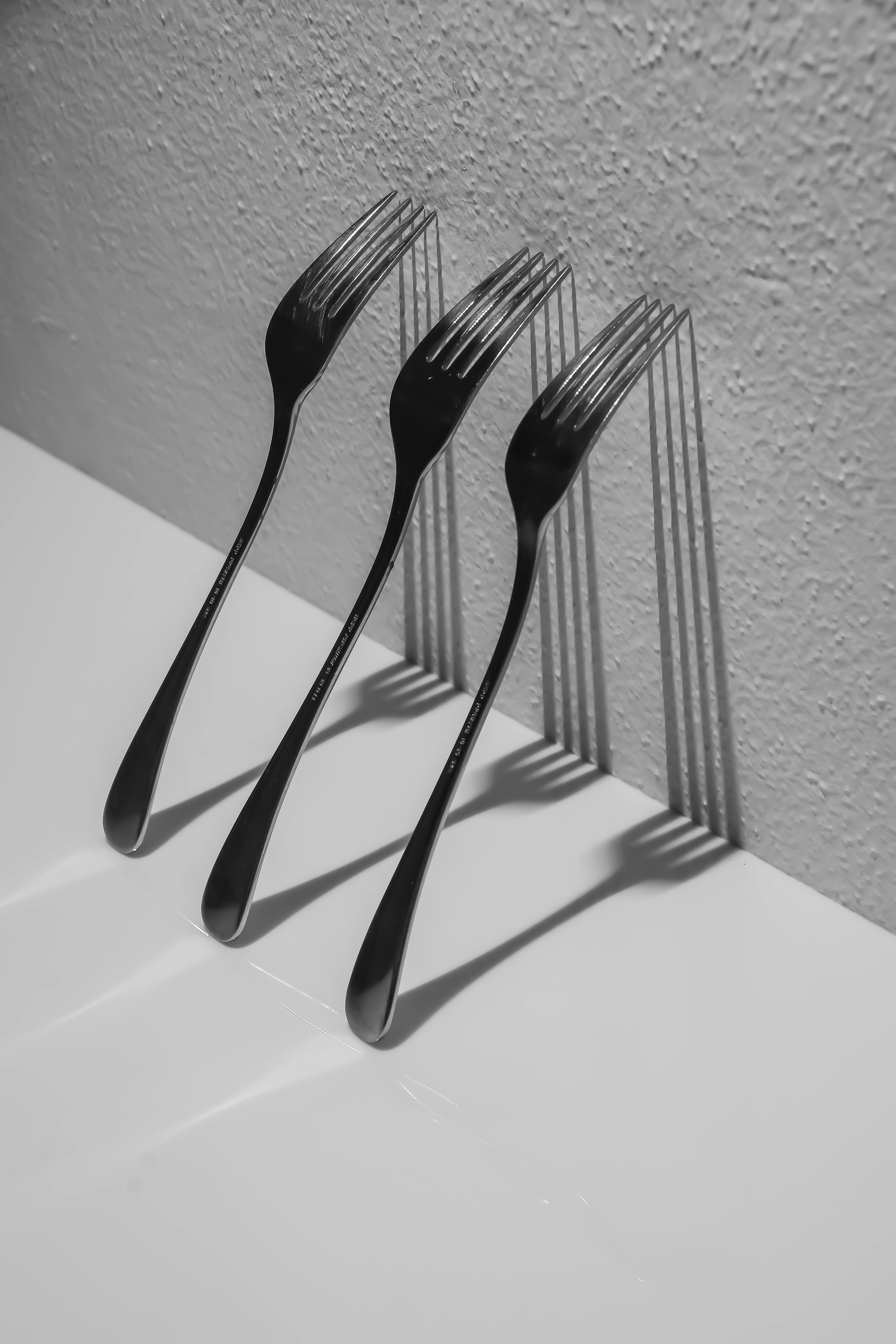 Free Three forks casting shadows on a table in an artistic black and white photo. Stock Photo