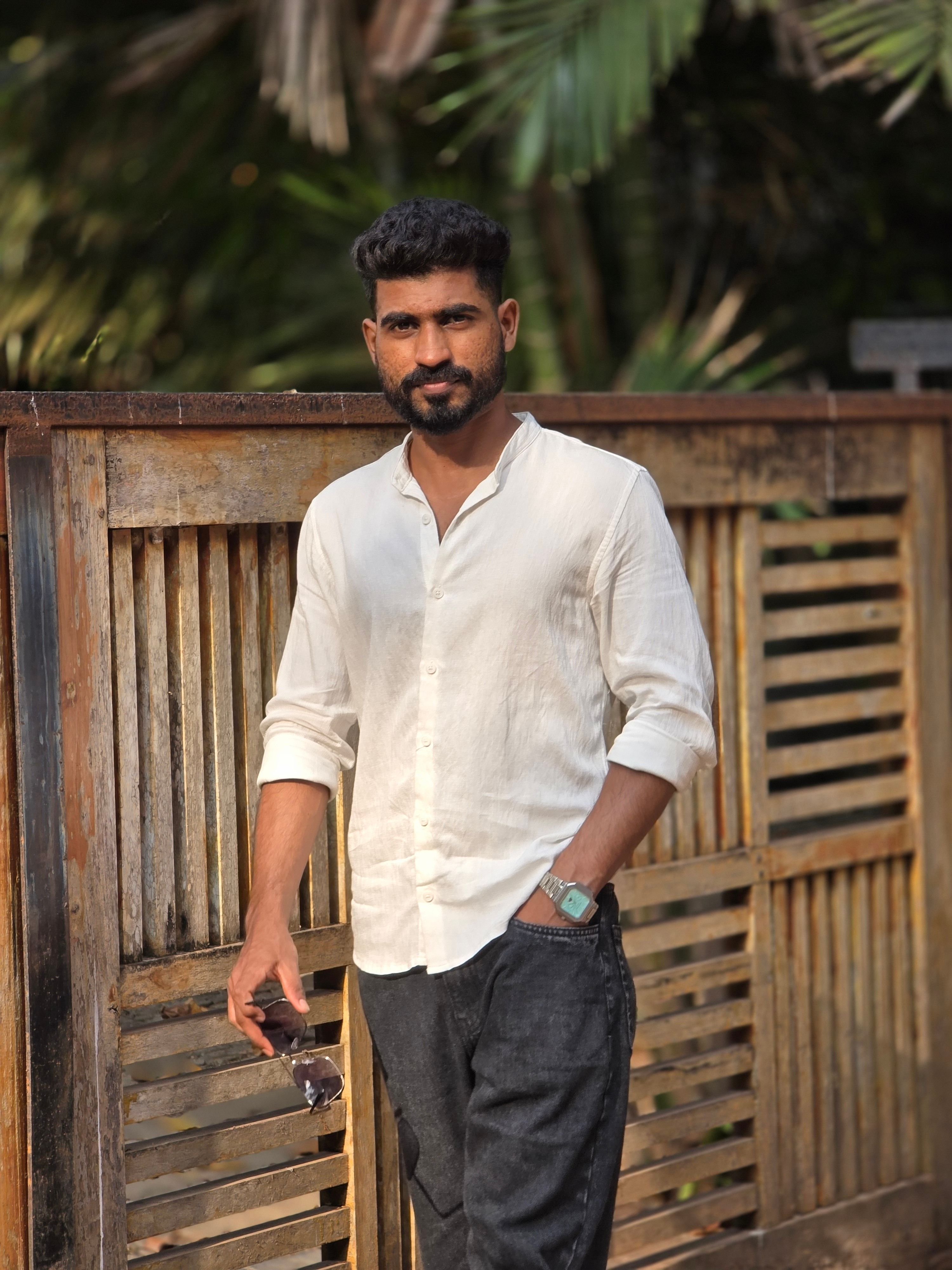 Man in casual white outfit leaning against wooden fence outdoors.