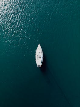 A tranquil aerial shot of a white sailing boat cruising on the turquoise Aegean Sea, perfect for travel and adventure themes.