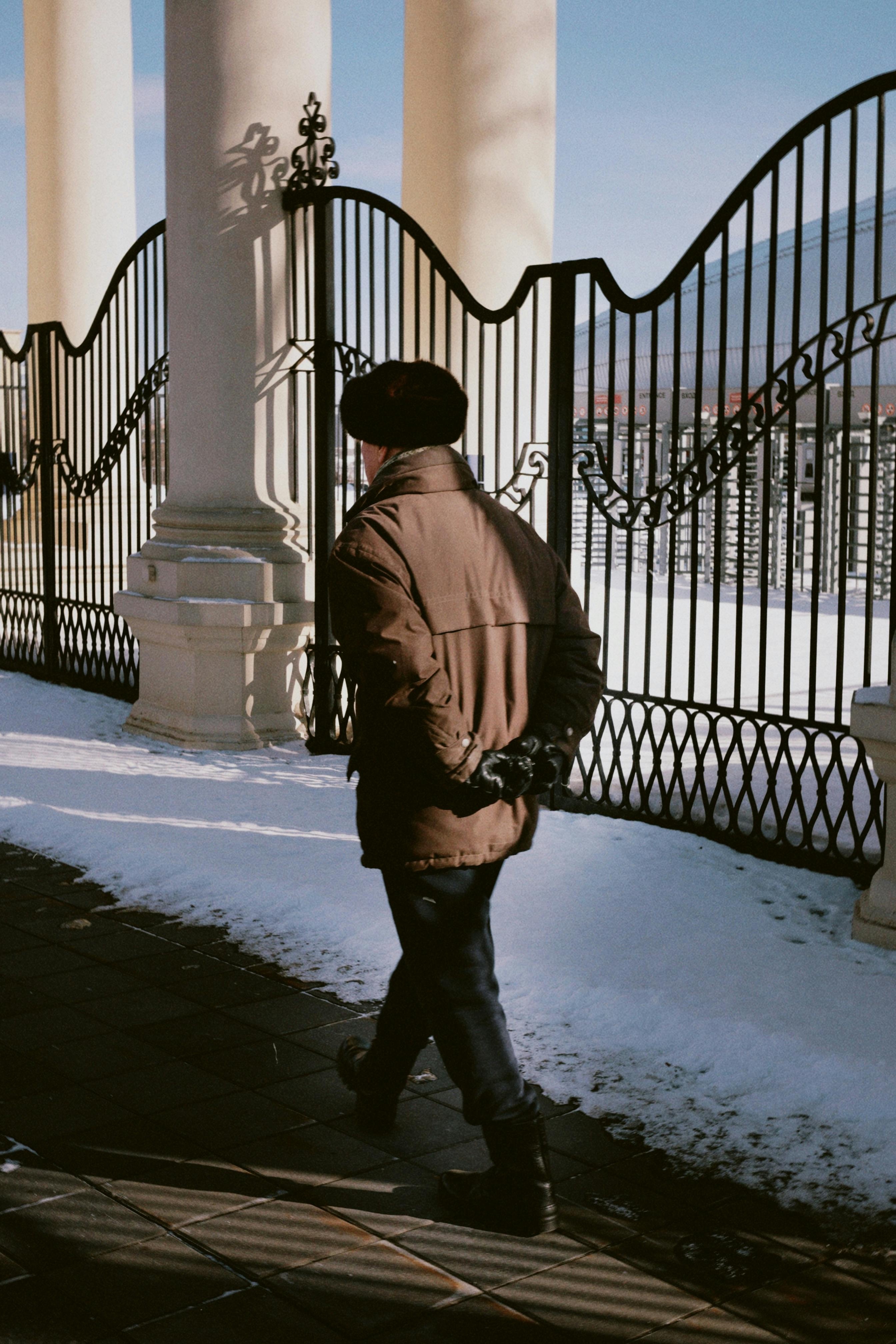 無料 日中、雪が降る都会の風景の中で、装飾的な鉄の柵のそばを歩く男性。 写真素材