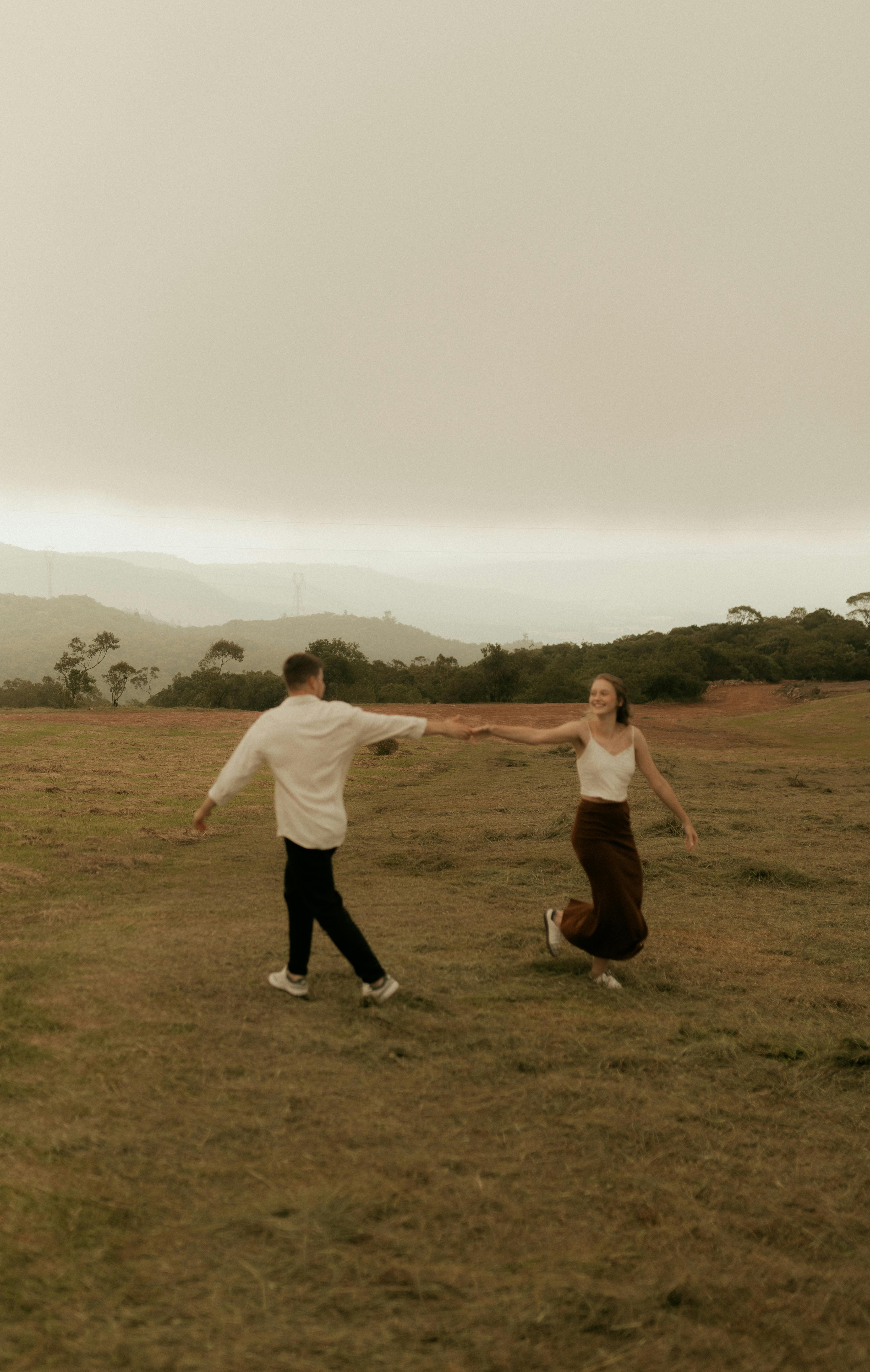 無料 穏やかな曇り空の下の静かな野原で、カップルが楽しそうにくるくる回っています。 写真素材