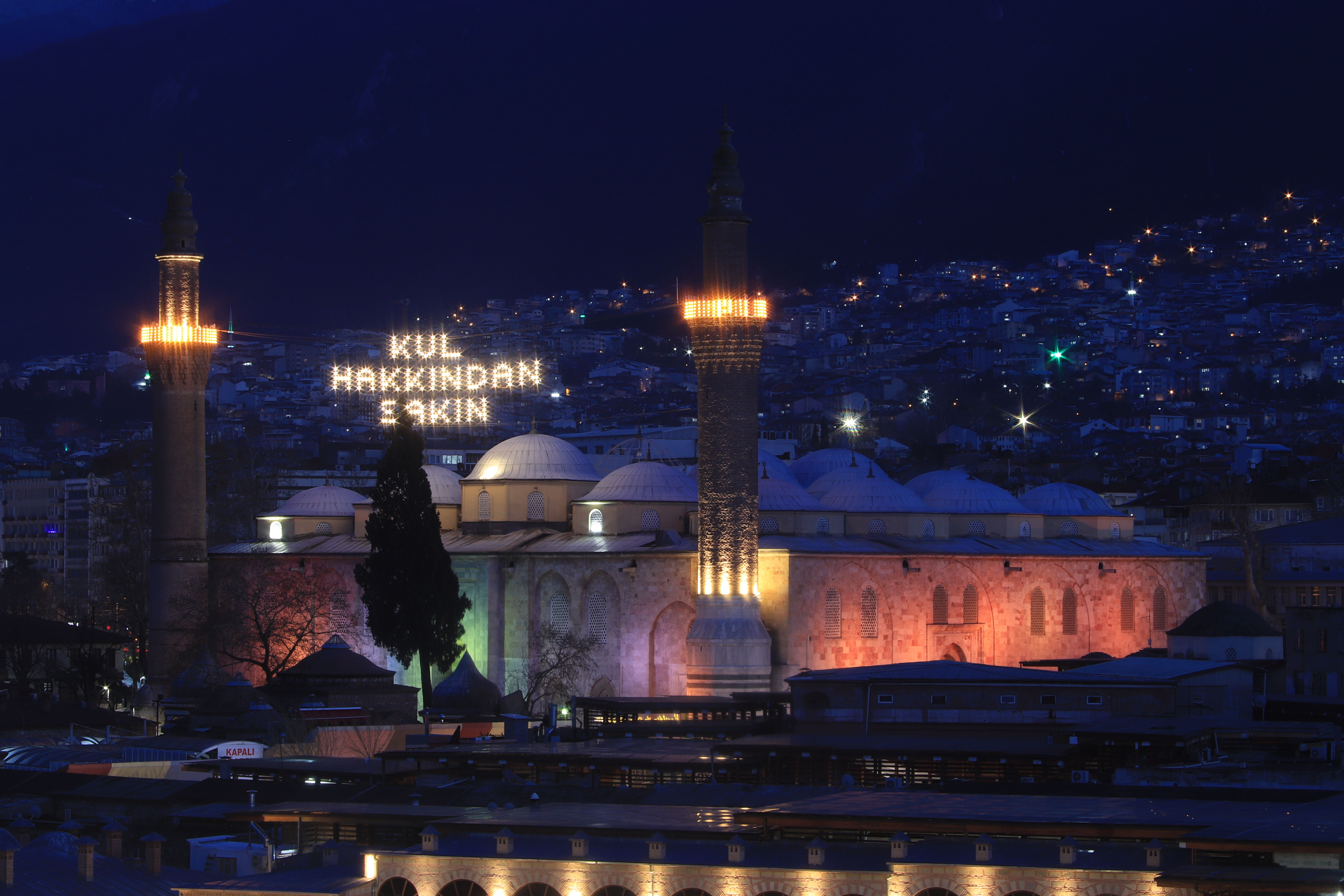 Illuminated Grand Mosque at night in Bursa, Türkiye with cityscape backdrop.