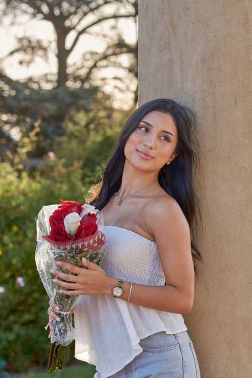 Free Young woman holding a bouquet of red and white roses, enjoying a serene outdoor setting. Stock Photo