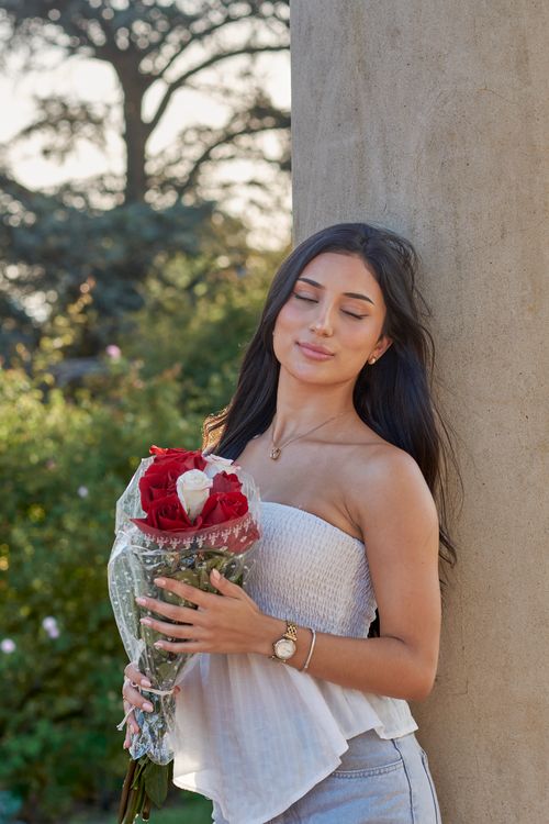 Free A young woman stands outdoors in Montevideo, holding a bouquet of red roses and smiling gently, against a natural backdrop. Stock Photo