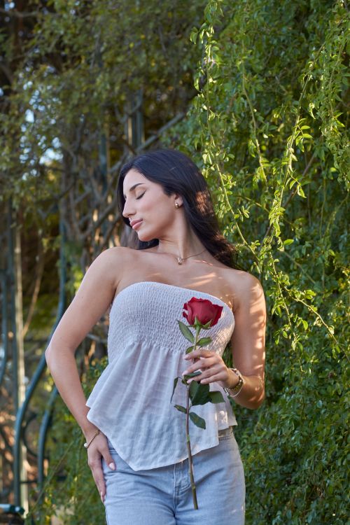 Free Portrait of a woman holding a red rose with green foliage background in a serene garden. Stock Photo