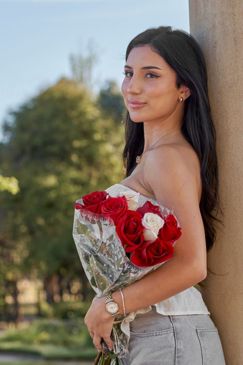 Free A young woman smiles while holding a bouquet of red and white roses outdoors. Stock Photo