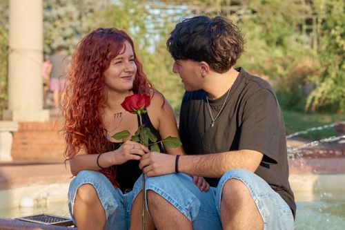 Free A young couple shares a romantic moment holding a rose by a fountain in Montevideo, Uruguay. Stock Photo