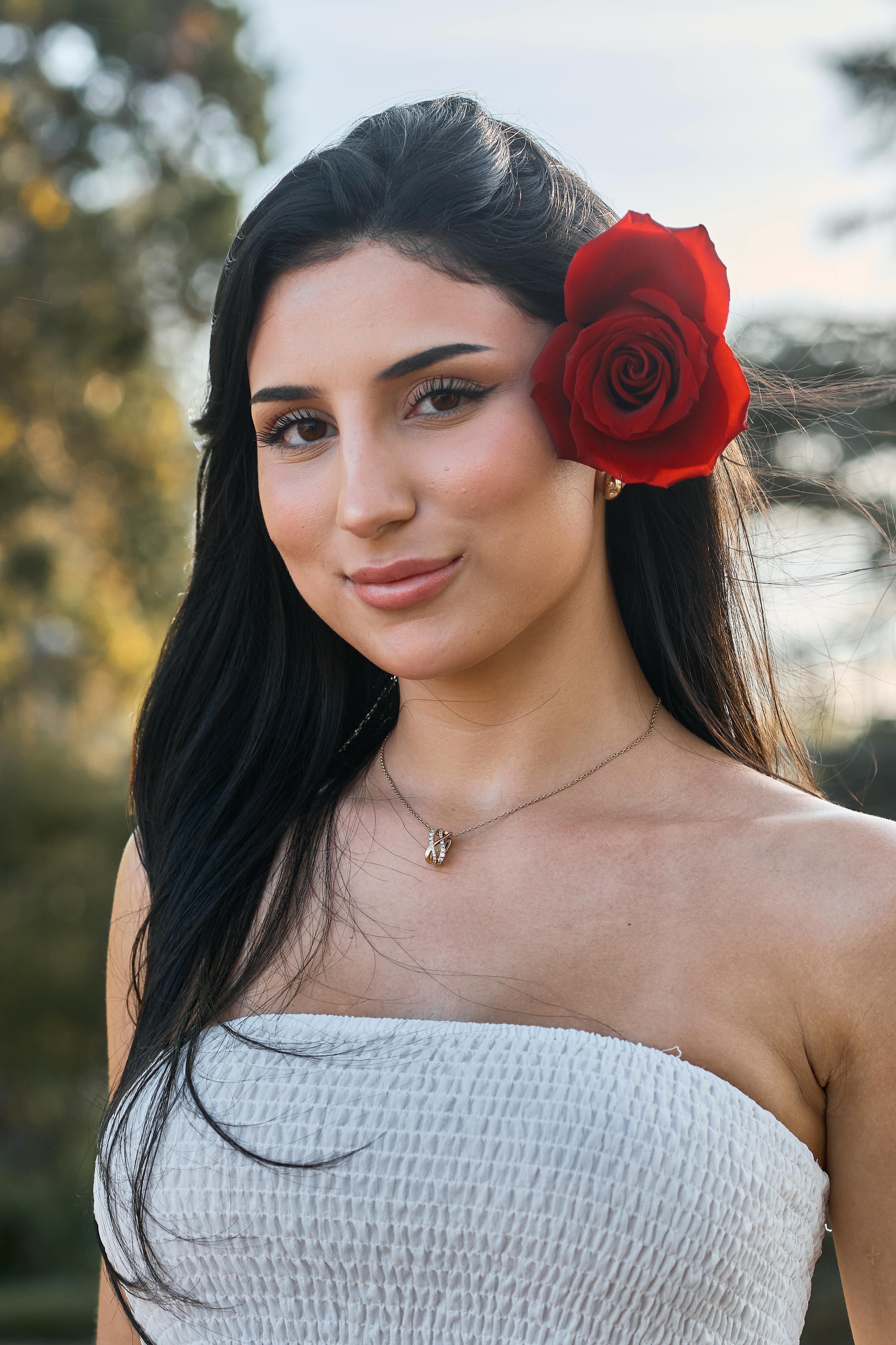 Free Portrait of a young woman with a red rose in her hair, smiling outdoors in Montevideo. Stock Photo