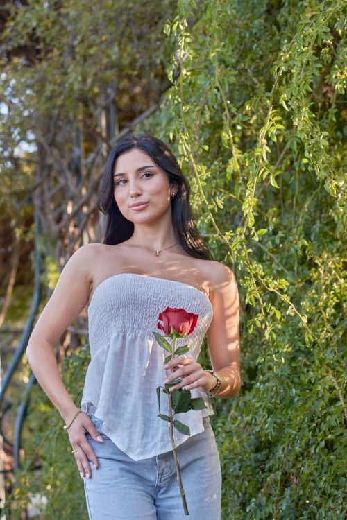 Free A young woman stands outdoors in Montevideo holding a red rose, surrounded by lush greenery. Stock Photo