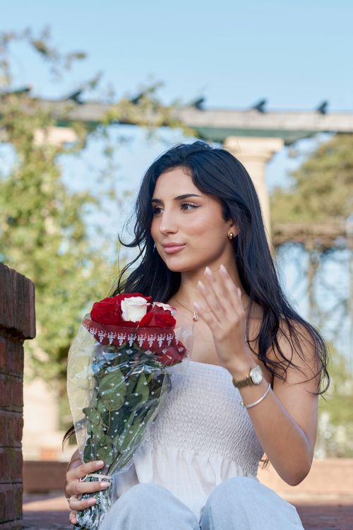 Free Young woman holding red roses against Montevideo's scenic backdrop, showcasing casual elegance. Stock Photo