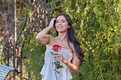 Free Smiling young woman with a red rose in a lush outdoor setting, capturing the essence of nature and joy. Stock Photo