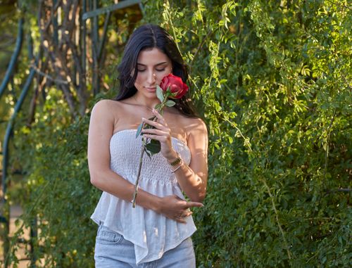 Free A young woman enjoys a serene moment with a red rose in a lush green garden. Stock Photo