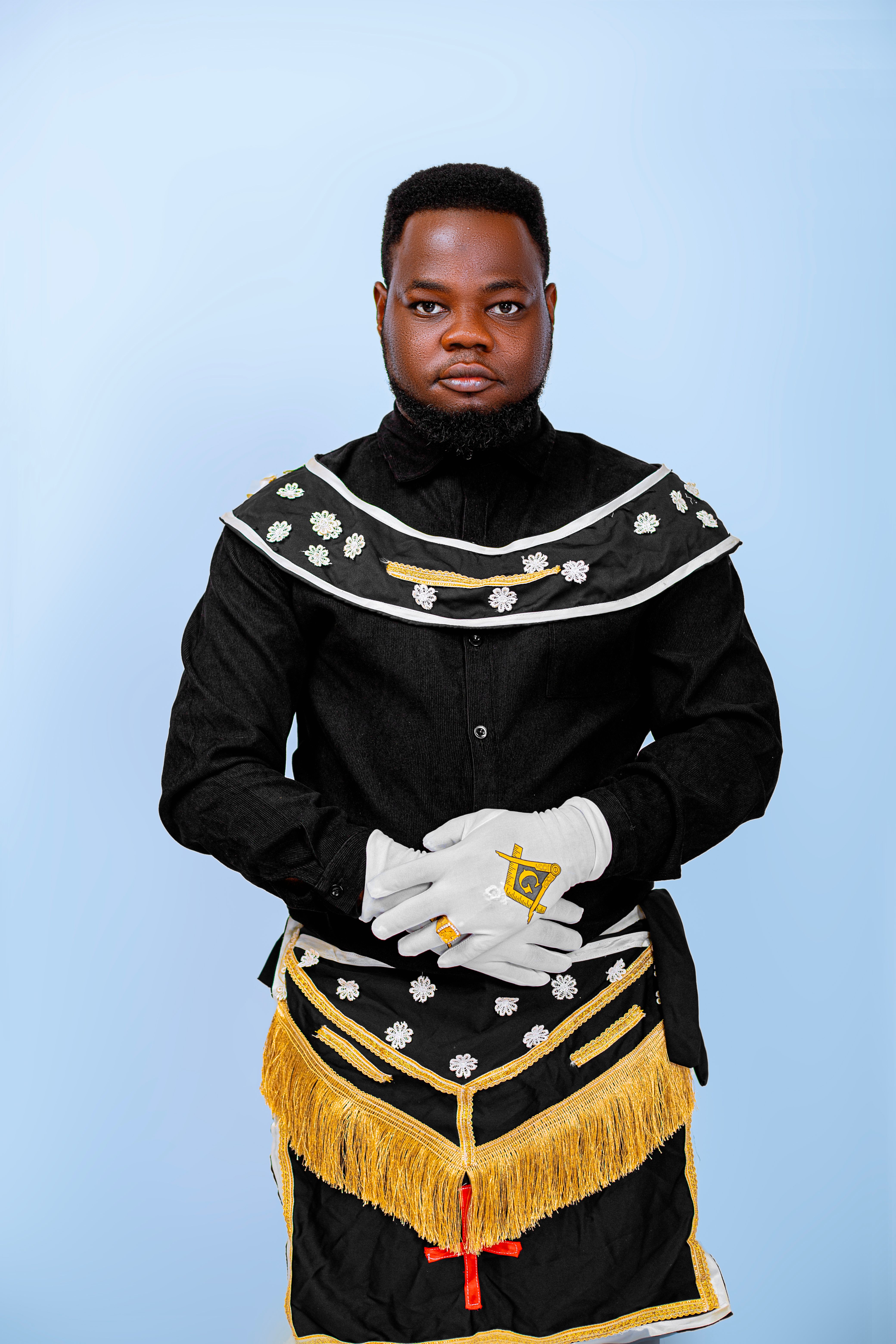 Portrait of an African man wearing elaborate traditional Freemason attire against a light blue background.