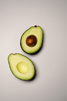 Two halves of a ripe avocado displayed on a neutral backdrop, highlighting texture and color.