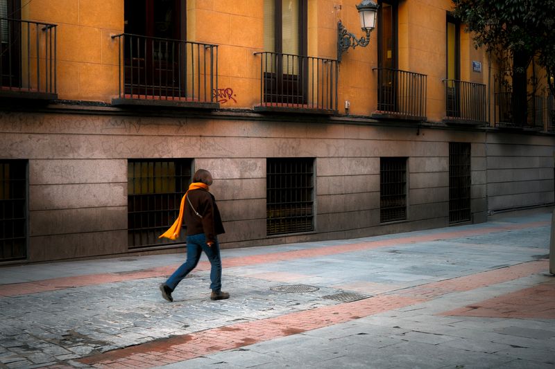 A woman walks in a colorful European street, capturing urban charm and solitude.