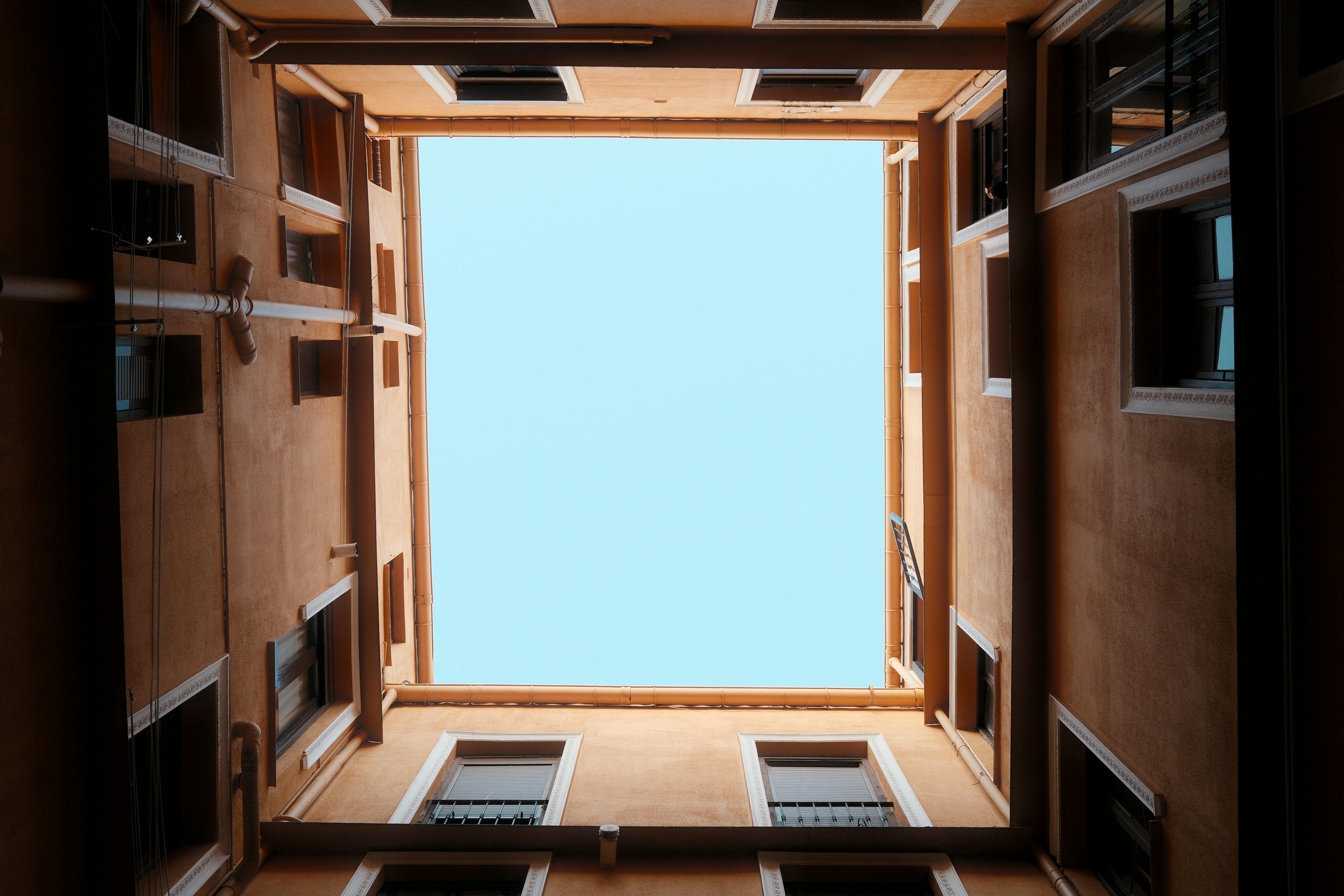 Free Looking up at blue sky framed by brown building walls of a courtyard. Stock Photo