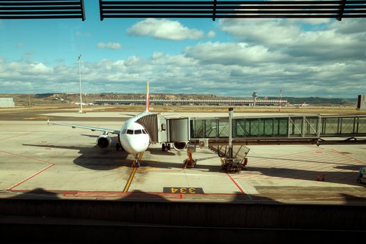 A commercial airplane docked at an airport gate under a blue sky with clouds.