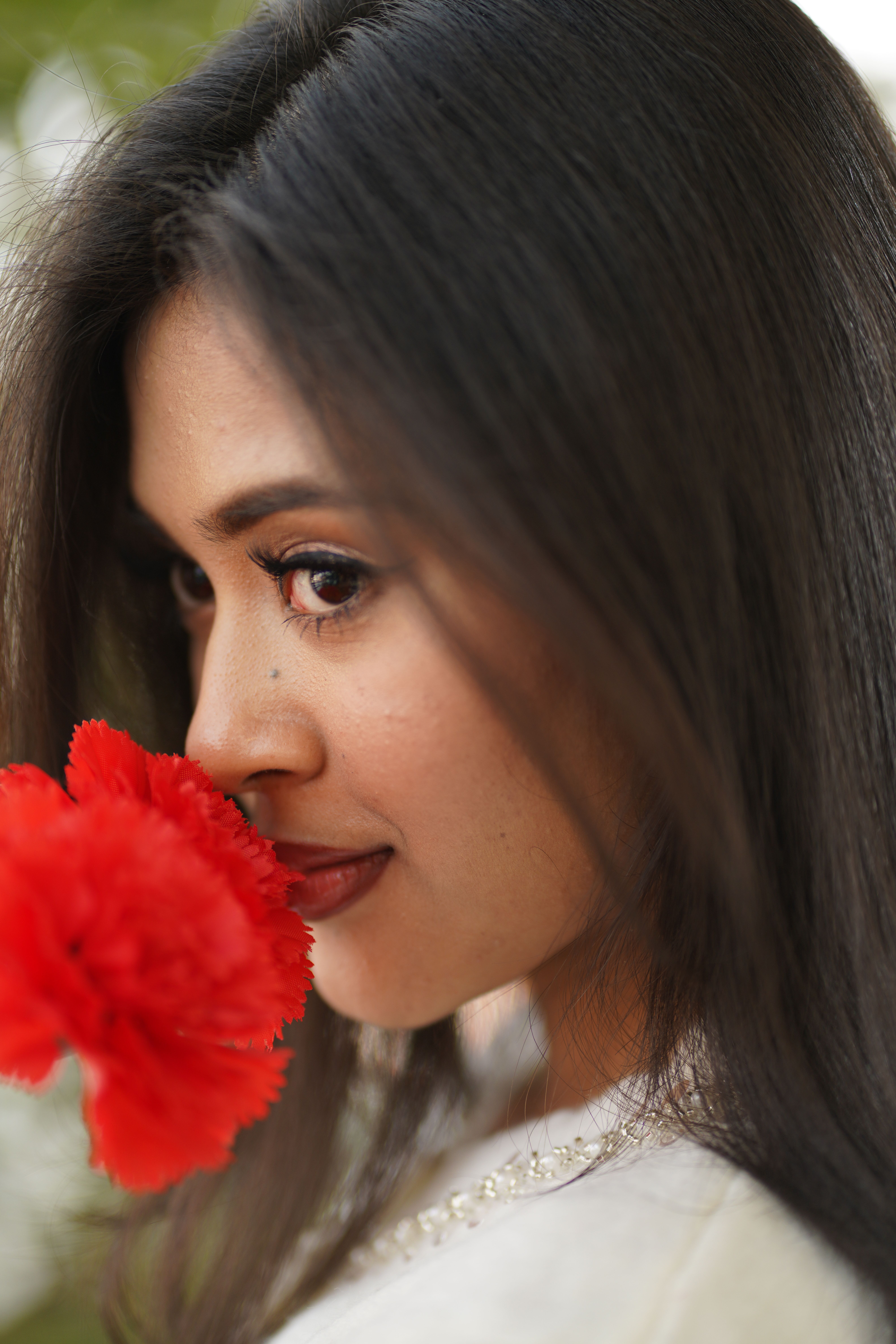 Close-up portrait of a woman gazing at a vibrant red carnation, creating a serene moment.