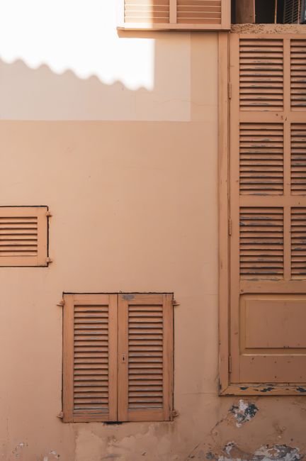 Warm-toned wooden shutters on a Mediterranean building facade in Artà, Spain.