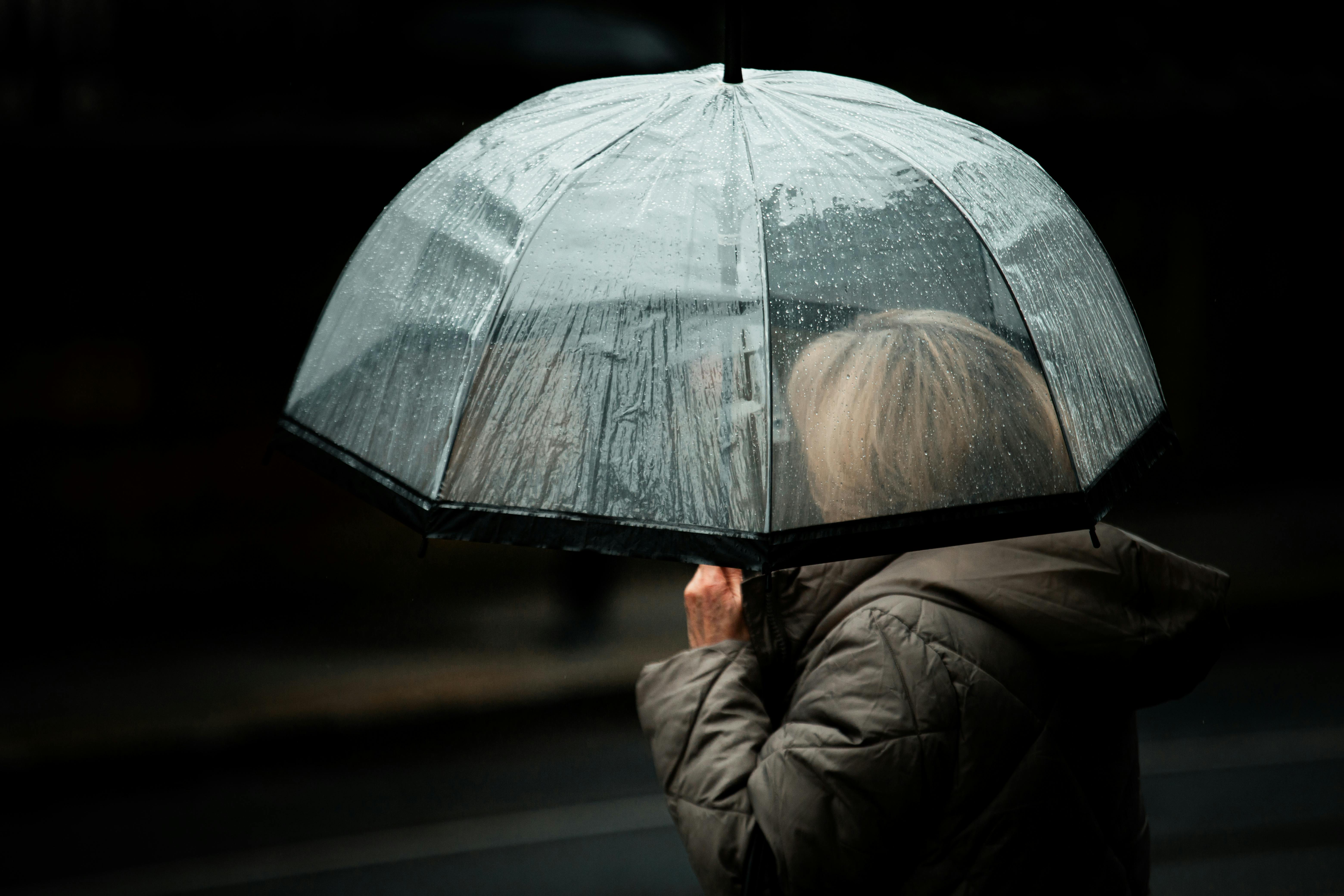 бесплатная Меланхоличная уличная фотография, запечатлевшая силуэт человека с прозрачным зонтом в дождливом Дублине. Стоковое фото