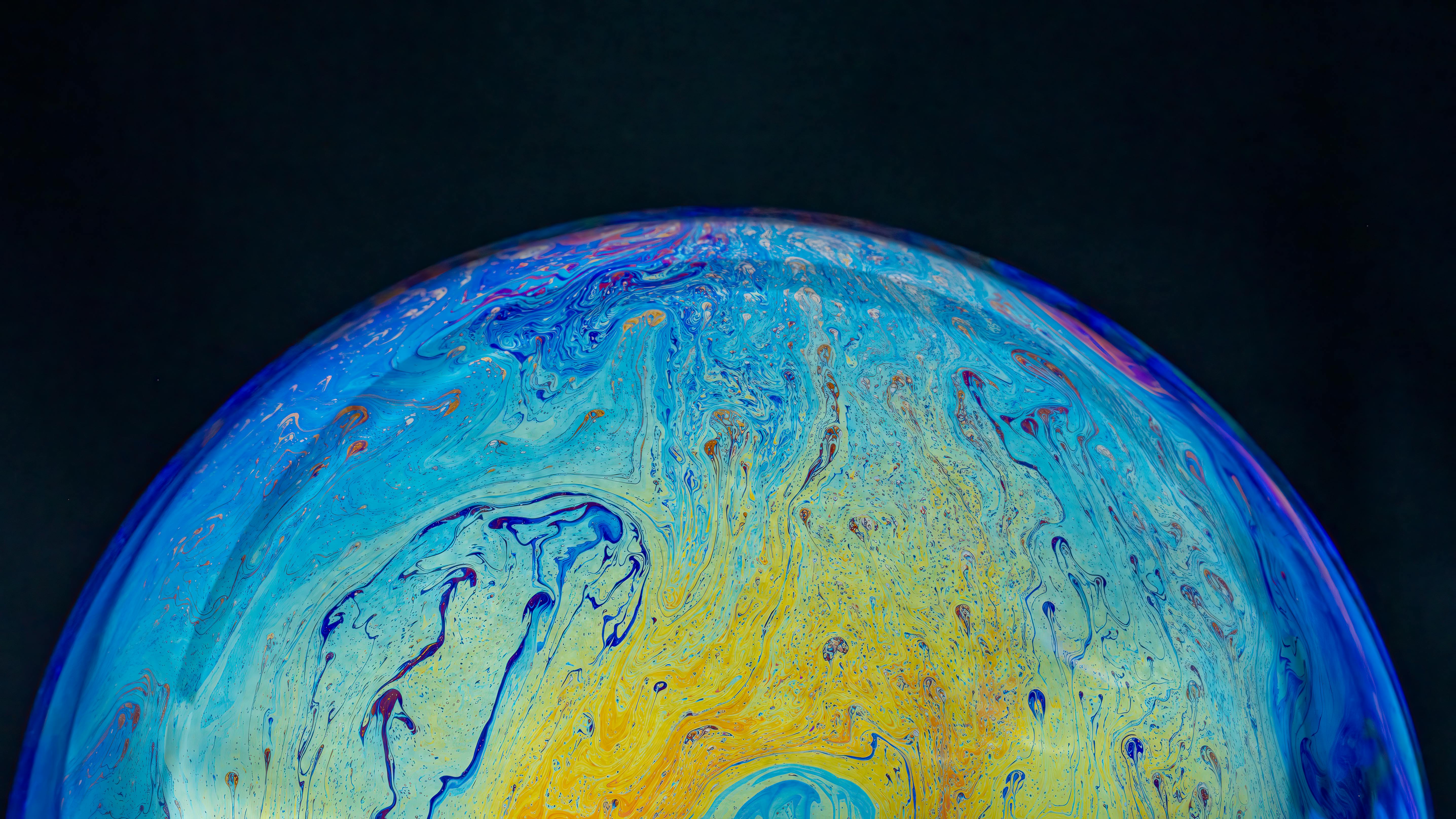 Free A close-up of a colorful soap bubble displaying vibrant iridescent hues against a black background. Stock Photo