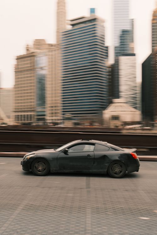 Free Black car in motion blur driving past urban skyscrapers, showcasing city vibes. Stock Photo